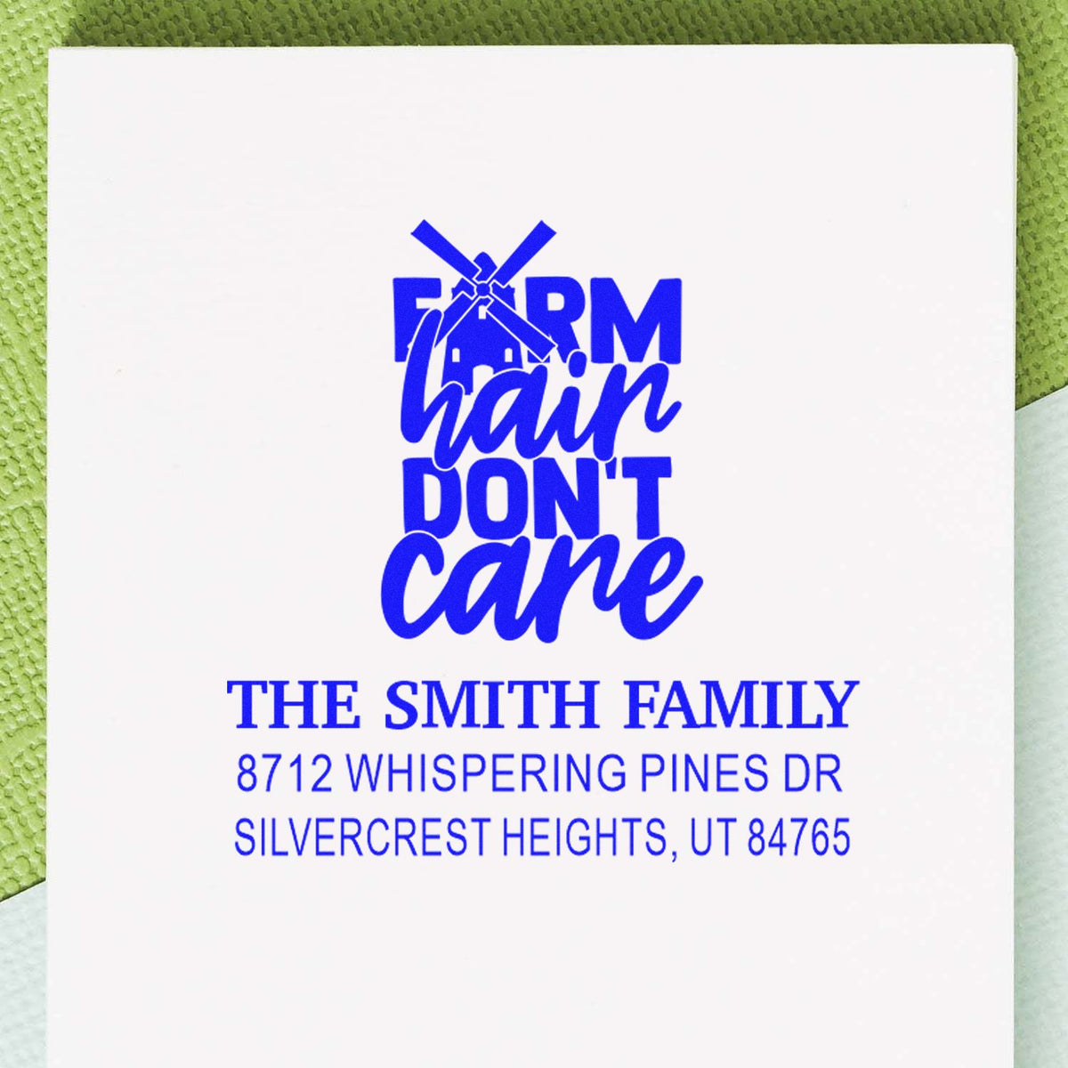 Custom blue address stamp with windmill and Farm hair dont care for The Smith Family, shown on white paper against a green textured background.