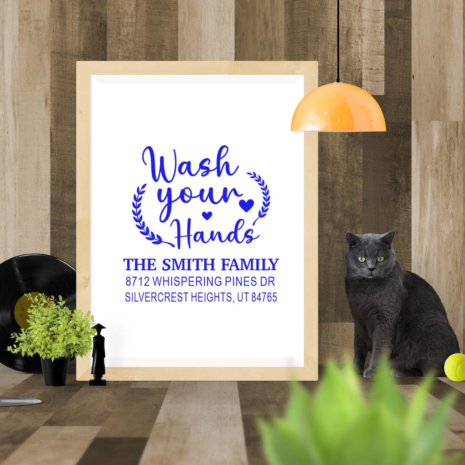 Custom family address stamp design with Wash your Hands on framed display, styled in rustic room with cat, plant, and lamp.