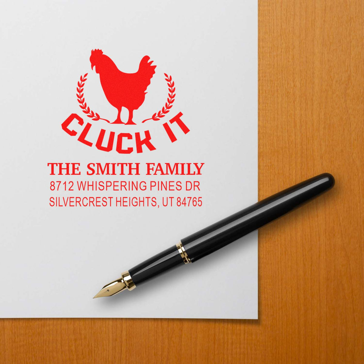Custom self-inking family address stamp with red rooster and Cluck It design on paper beside a fountain pen on a wooden desk.