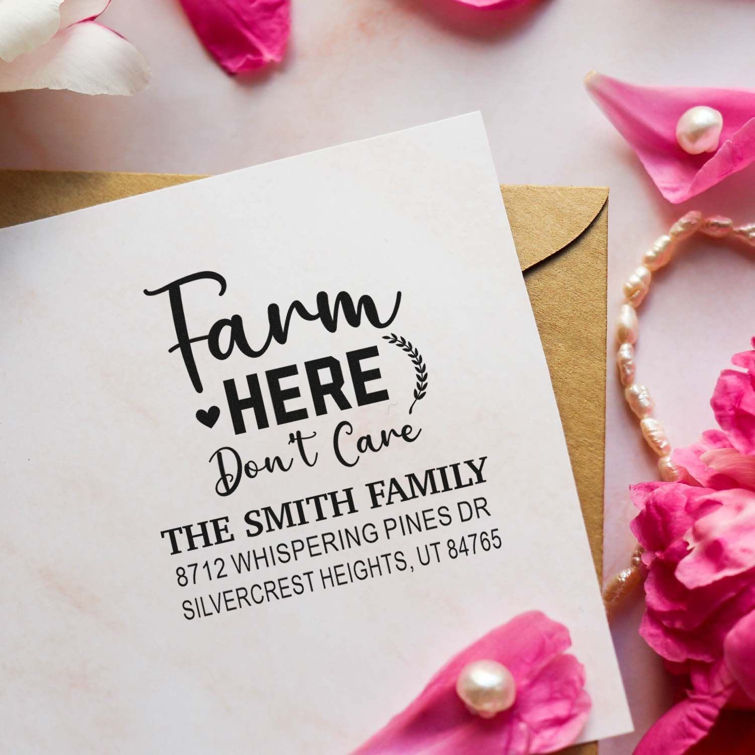 Custom farmhouse address stamp reading Farm Here Dont Care on white card, styled over kraft envelope with pink petals and pearls.