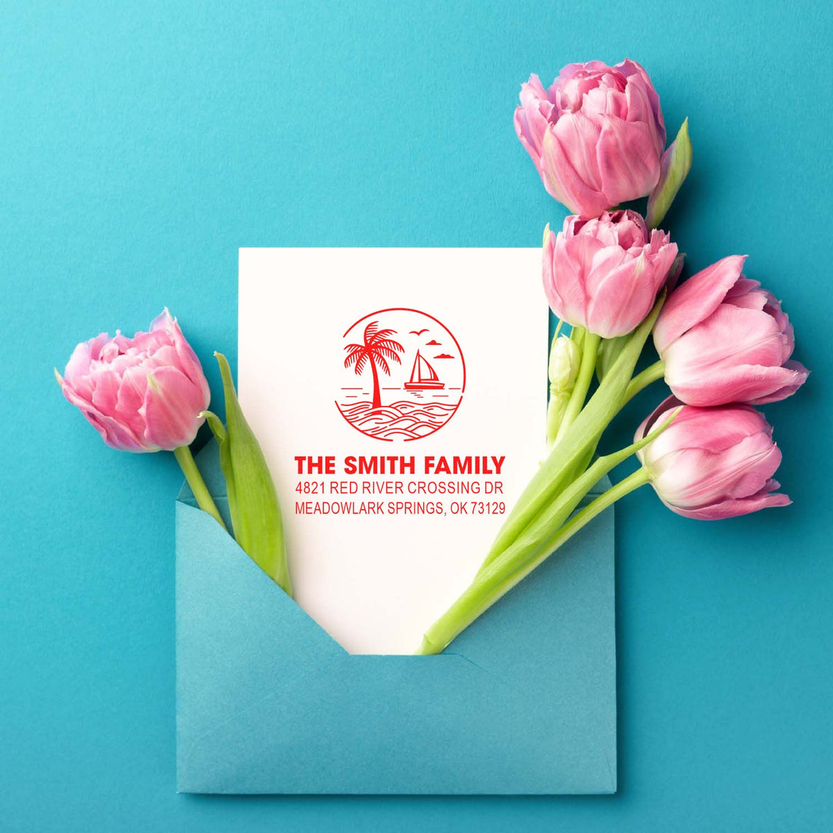 Custom family address stamp with tropical sailboat logo on a white card, tucked in a blue envelope with pink tulips on a teal background.