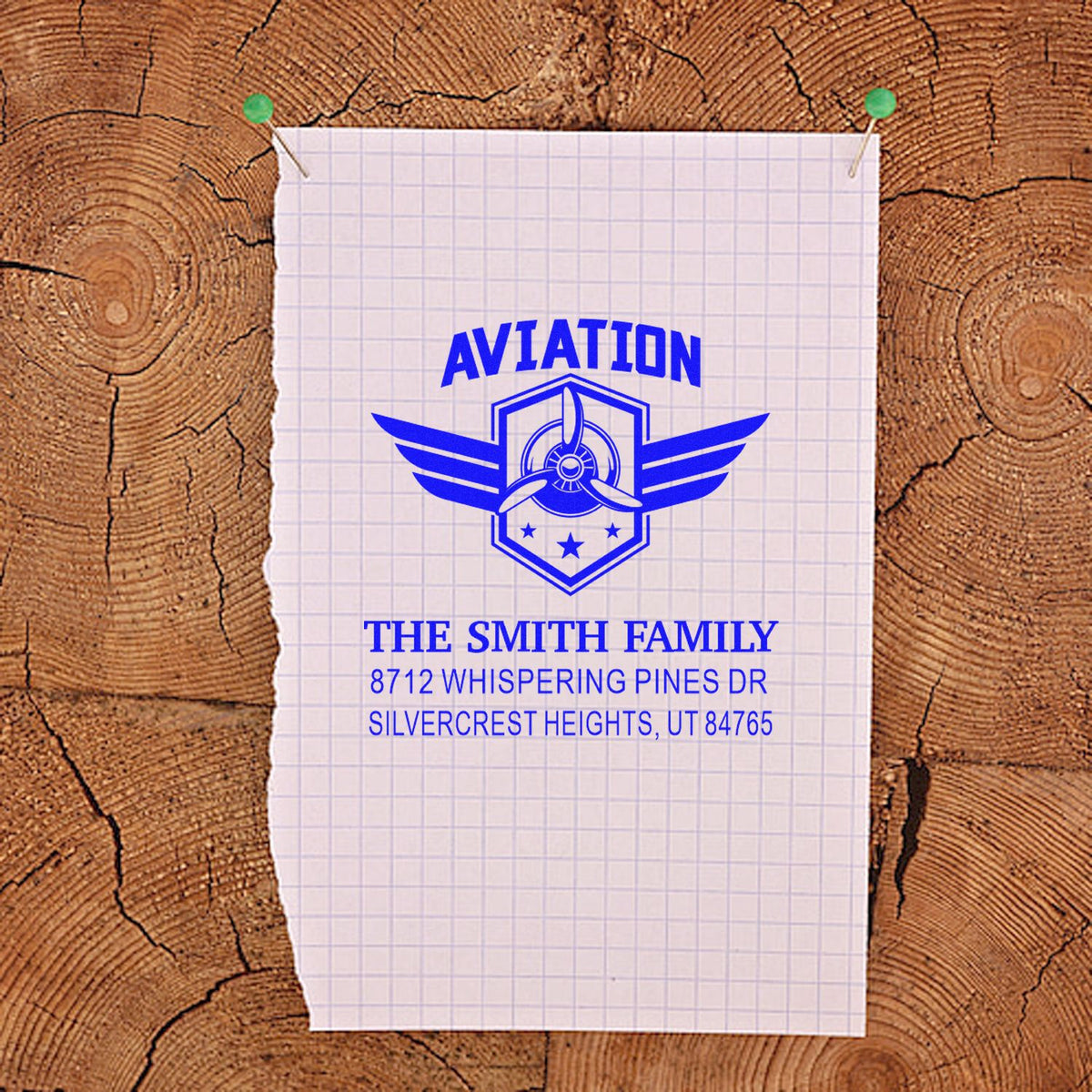 Custom aviation return address stamp with blue airplane emblem, The Smith Family name and address, pinned on graph paper over rustic wood.