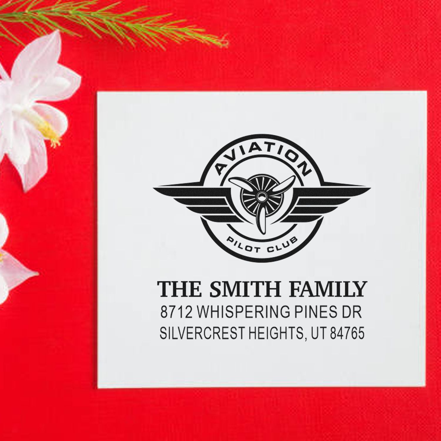 Personalized aviation pilot club address stamp for The Smith Family, shown on a white card over a red holiday background with flower and pine accents.