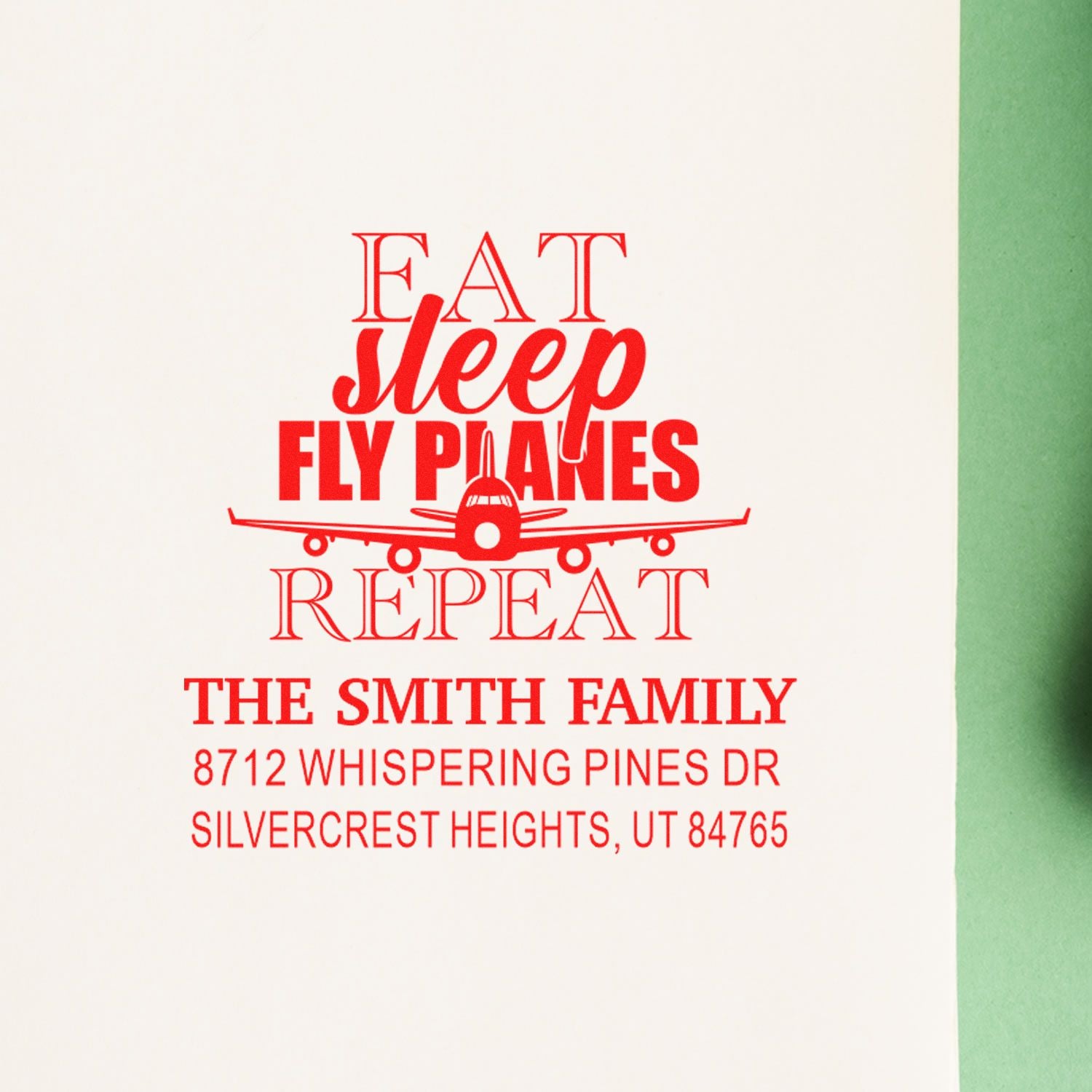 Red airplane-themed custom stamp reading Eat Sleep Fly Planes Repeat for The Smith Family, shown on white paper with green background.
