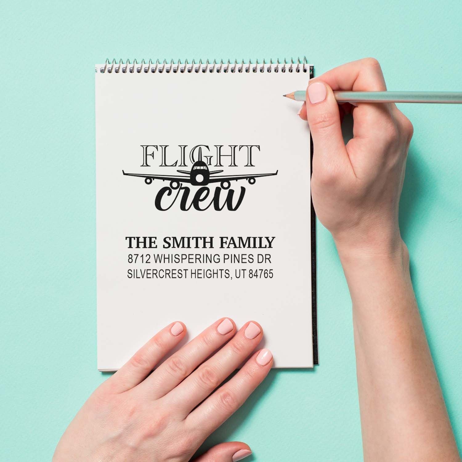 Custom Flight Crew airplane return address stamp on a notepad, held by hands with pencil on mint background.
