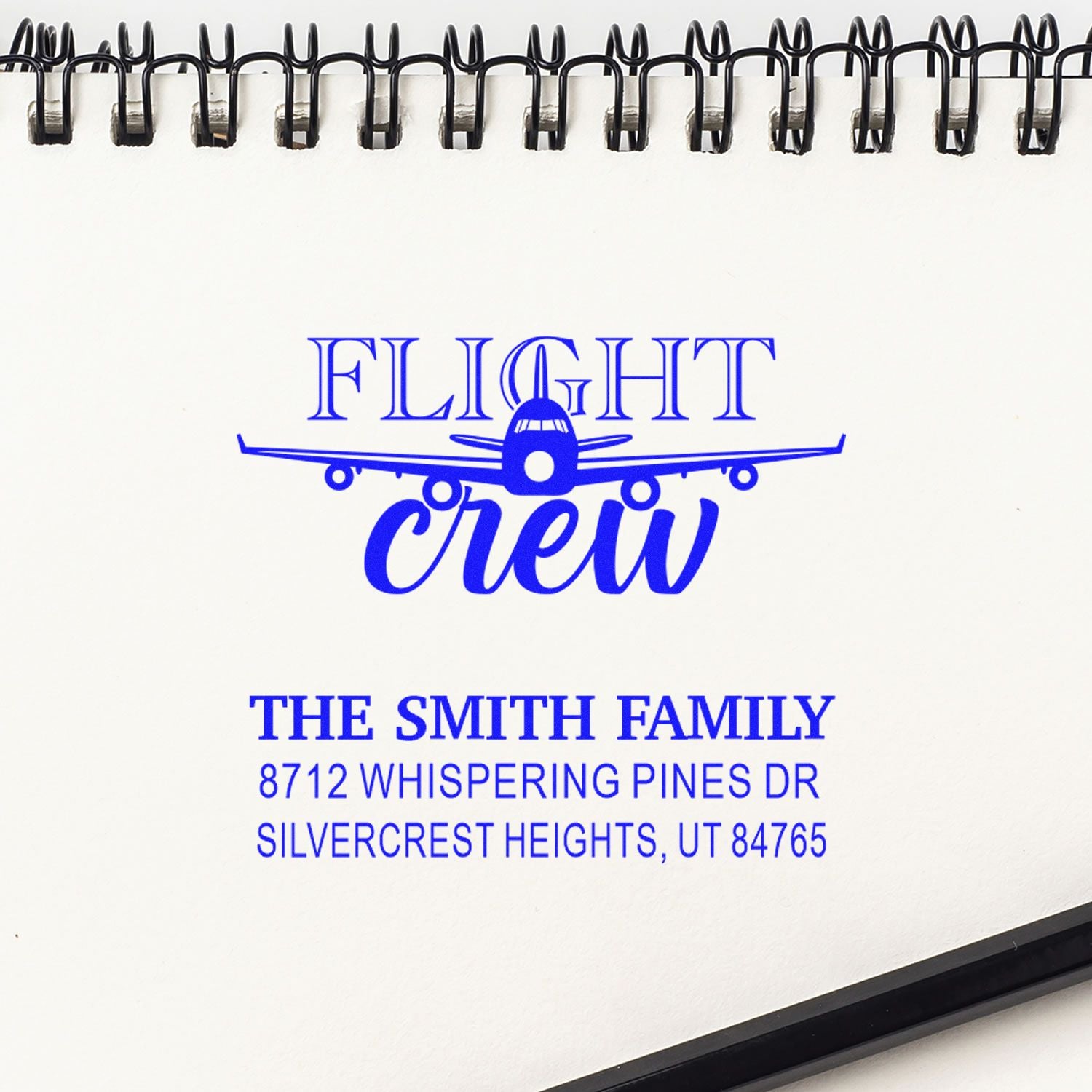 Blue Flight Crew custom address stamp with airplane graphic on a spiral-bound notebook, featuring The Smith Family address in Silvercrest Heights, UT.