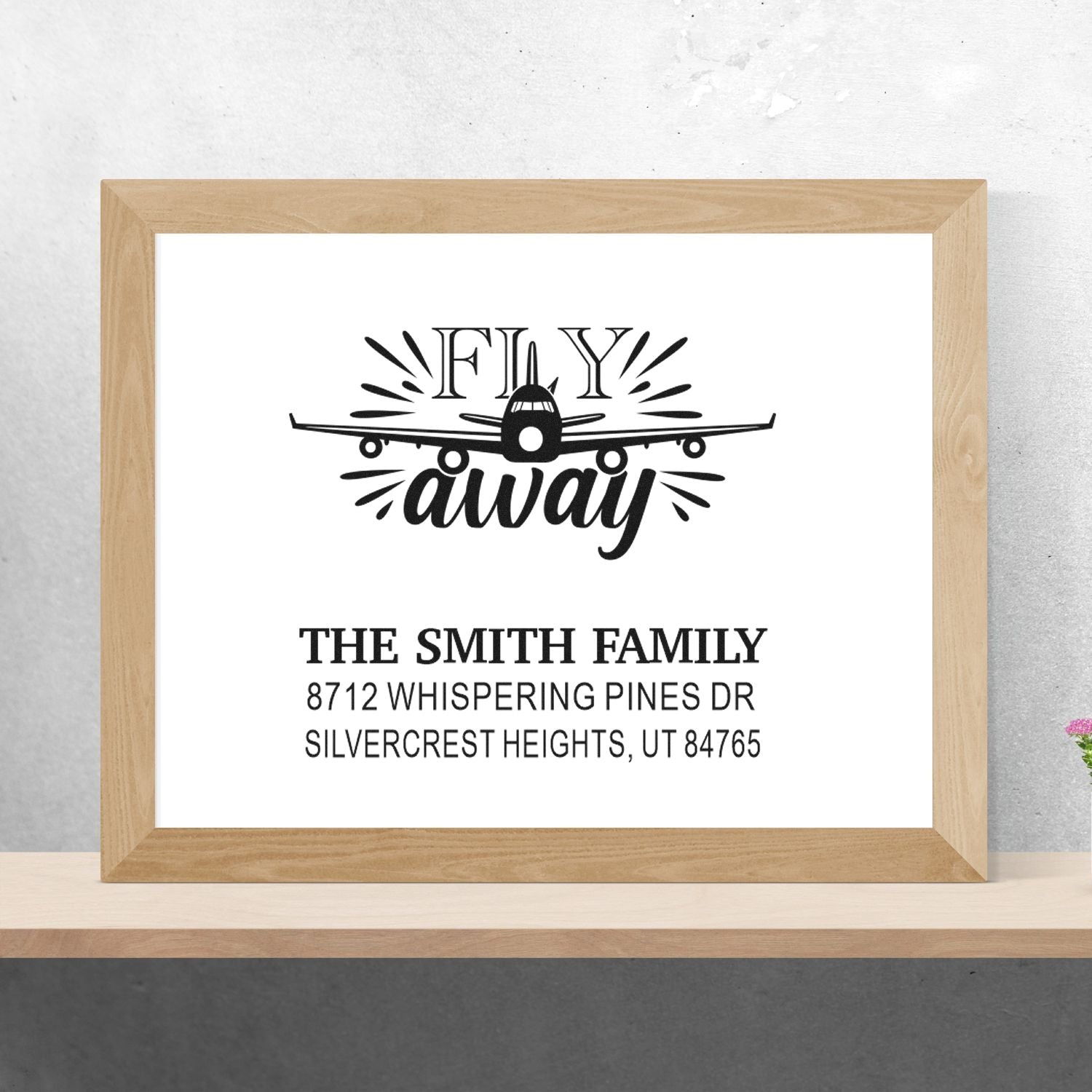 Custom Fly Away airplane family address stamp with The Smith Family name and mailing address, displayed in a wood frame on a shelf.