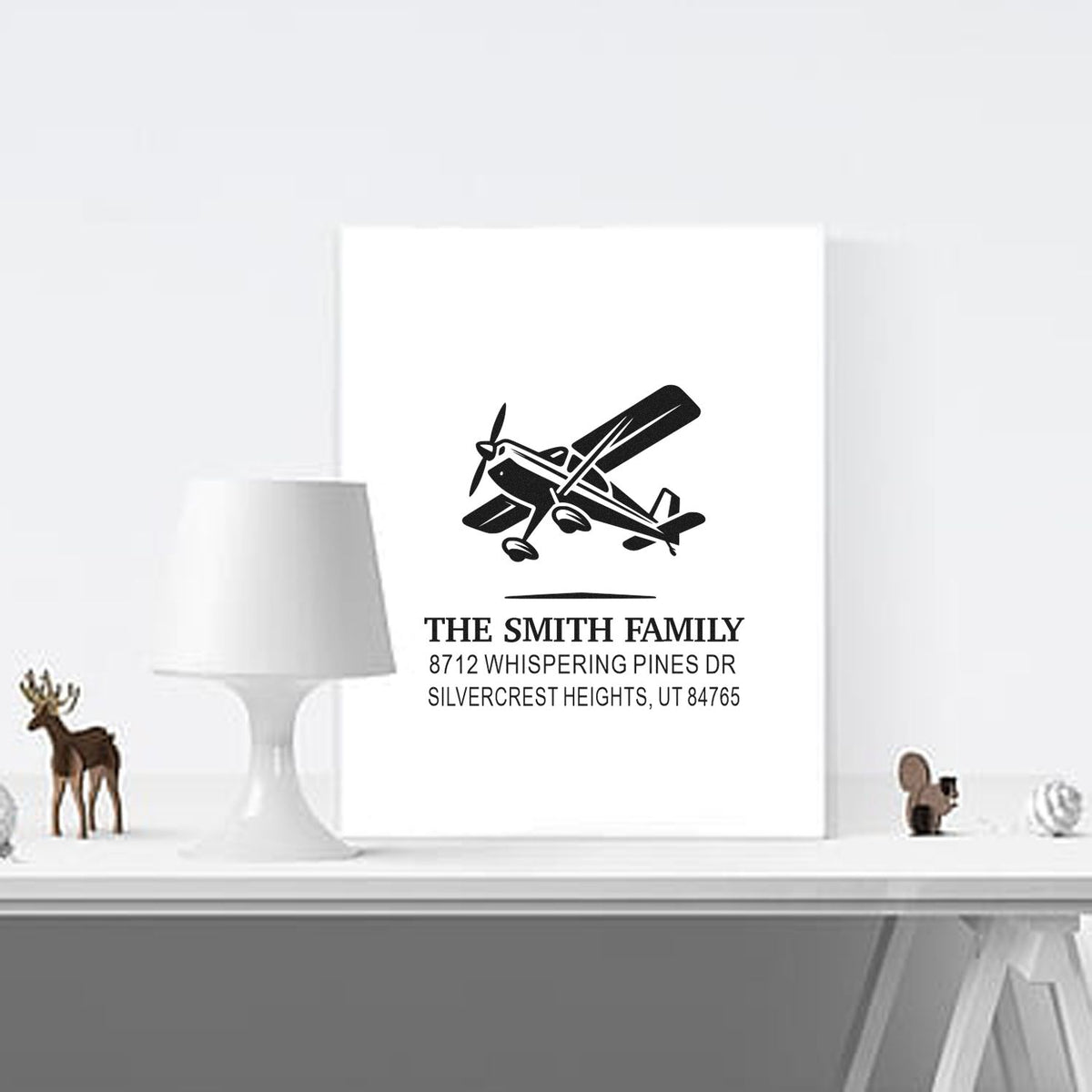 Custom family address stamp with airplane design, displayed on a white card in a minimalist home decor setting.