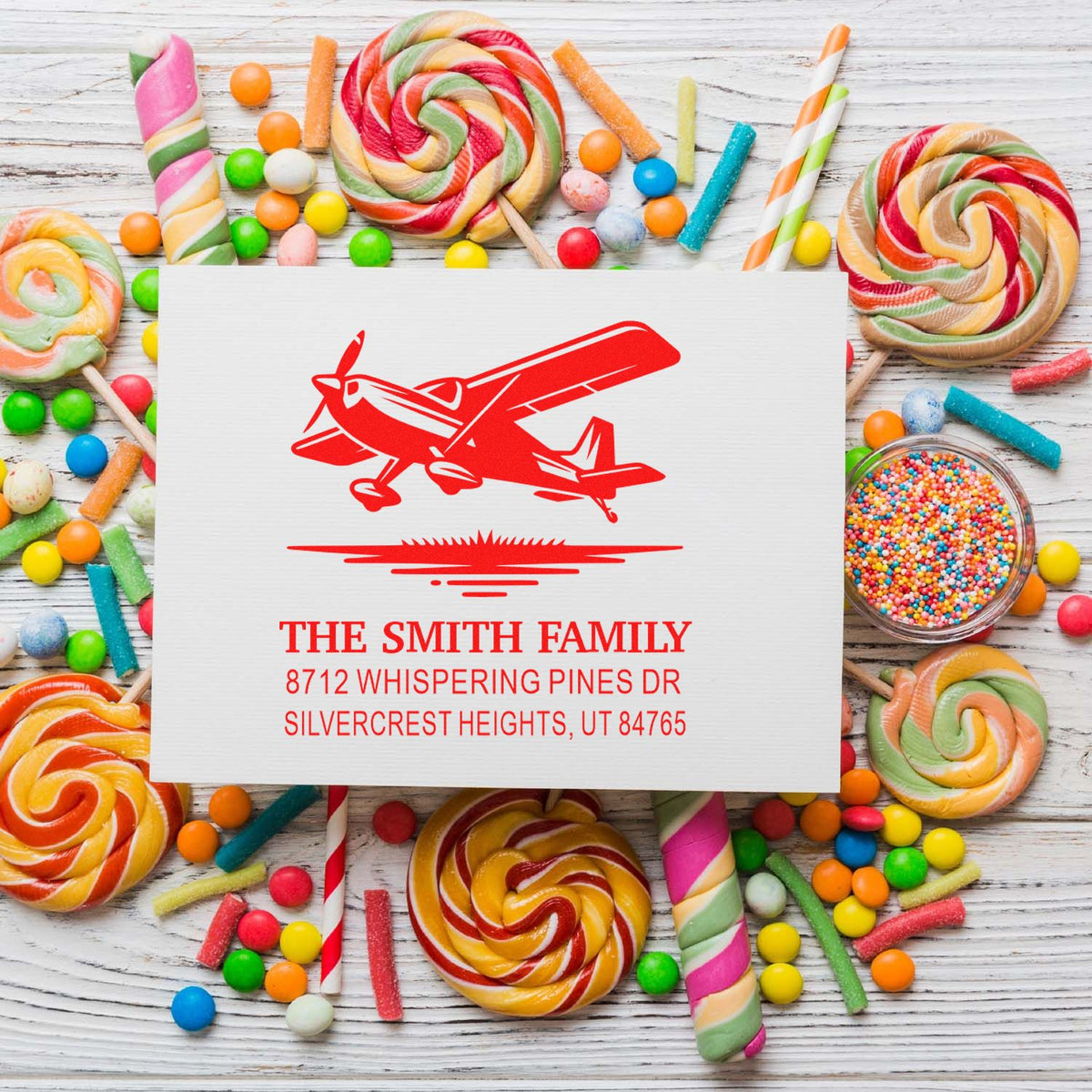 Custom airplane return address stamp with The Smith Family on a white wooden table surrounded by colorful candy lollipops and sweets.