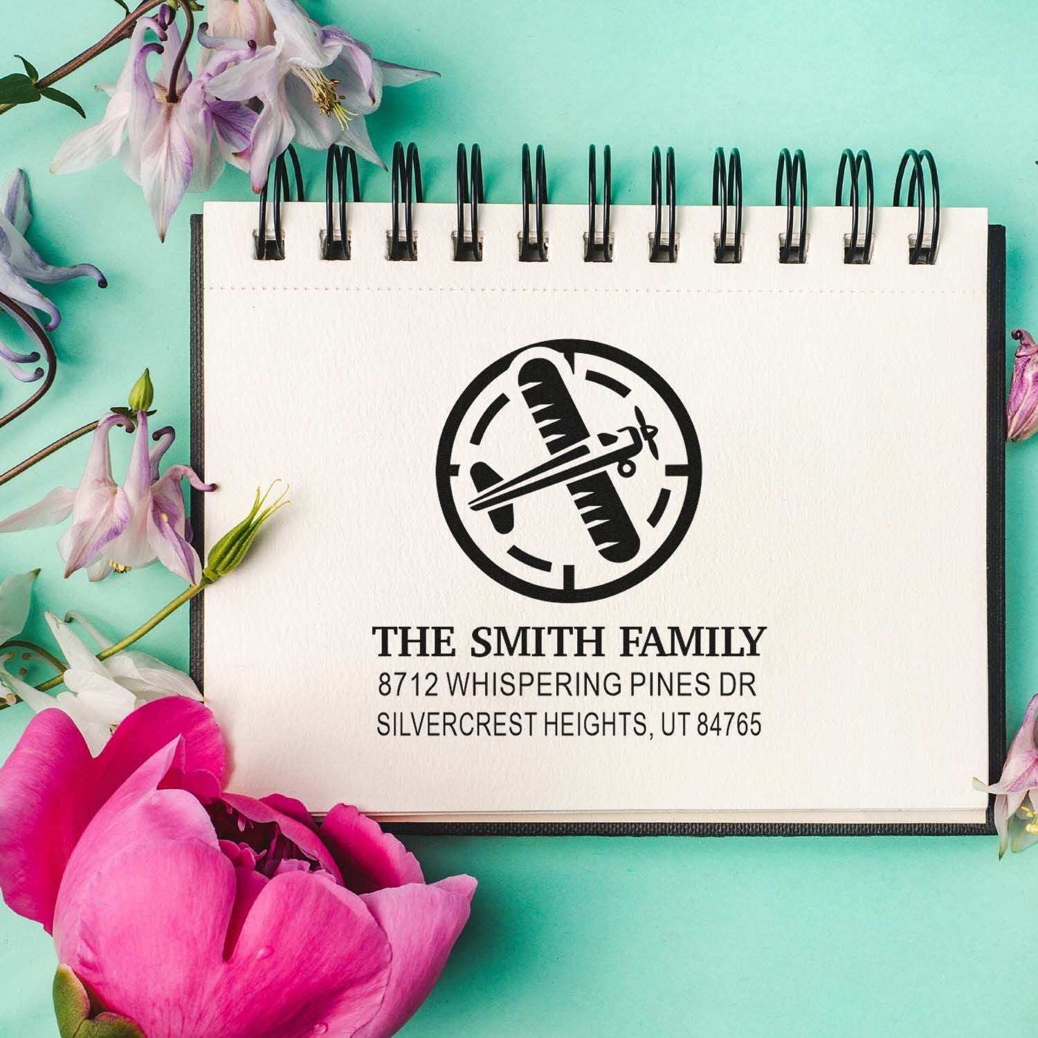 Custom family address stamp on spiral notepad with floral accents, featuring a crossed-airplane monogram and Smith family name.