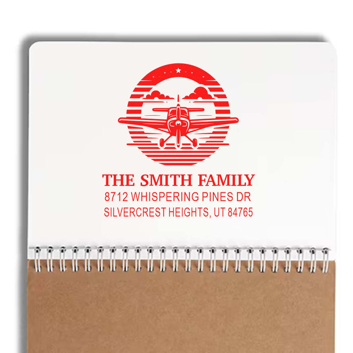 Custom red family address stamp with airplane logo reading The Smith Family, shown on a spiral notebook mockup.