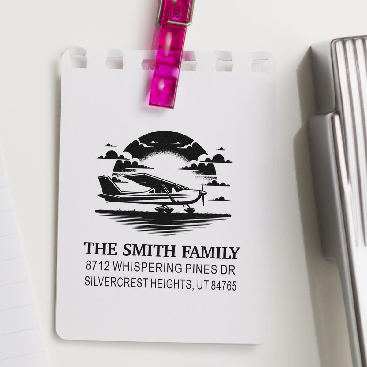 Custom return address stamp with airplane design for The Smith Family, clipped to a white display card beside a silver stamp holder.