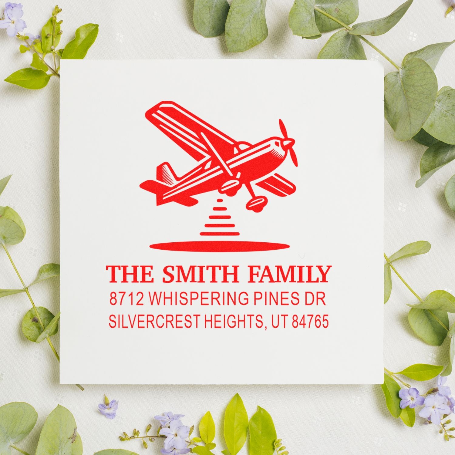 Custom return address stamp with red airplane design on white card, styled on a floral background.