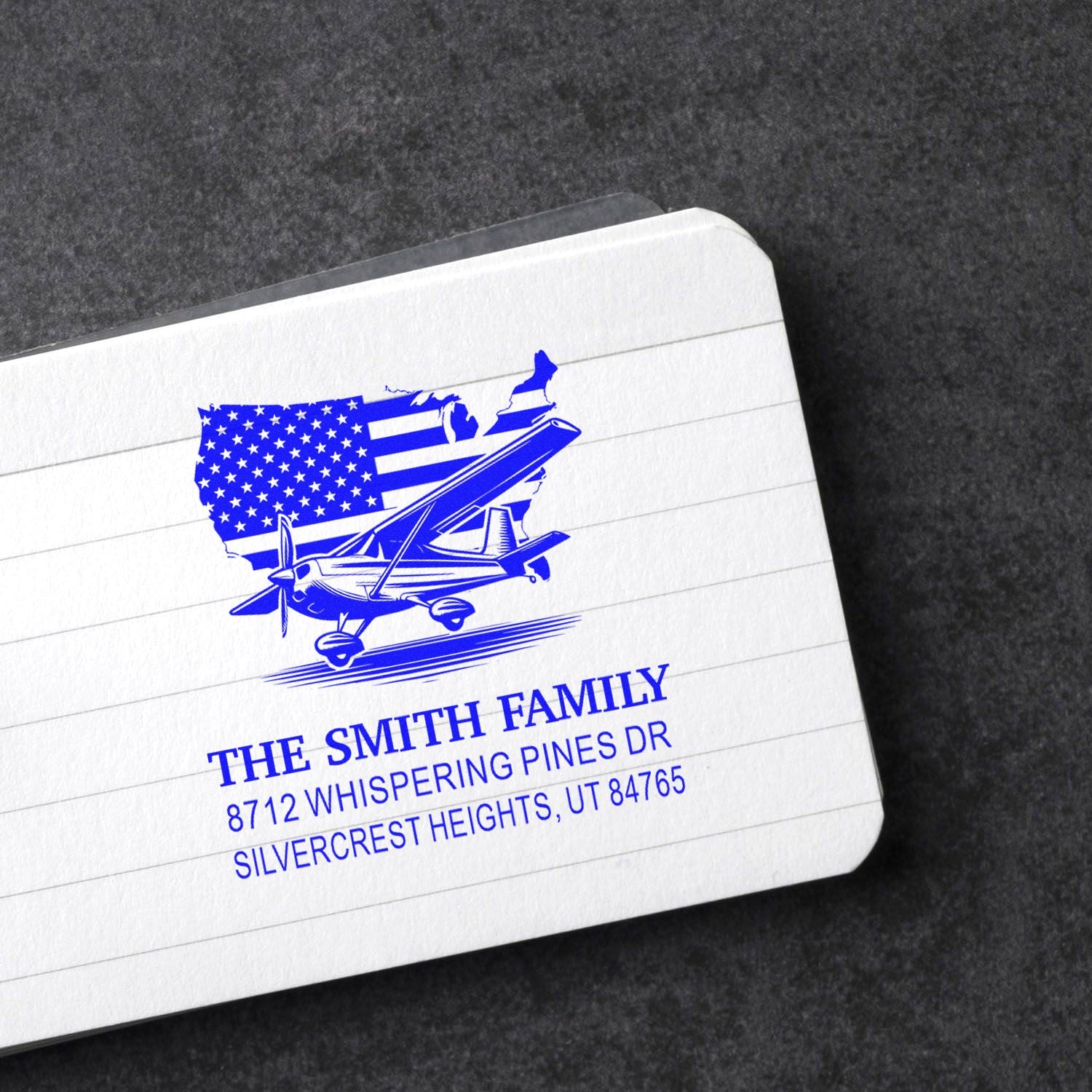 Custom self-inking address stamp with U.S. map and airplane design for The Smith Family, shown on a lined white card against a dark background.