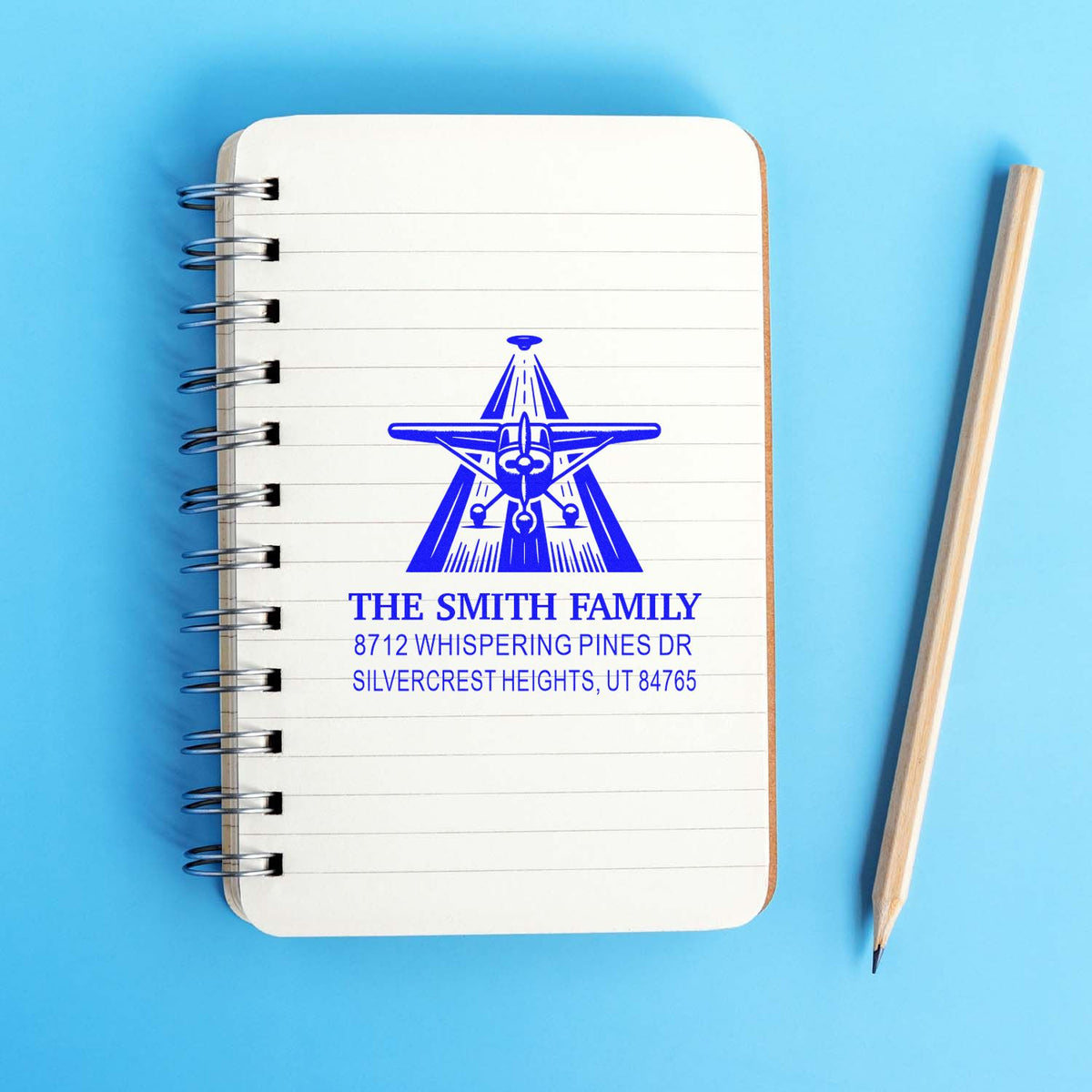 Personalized blue return address stamp for The Smith Family on a spiral notebook, with pencil on a blue background.