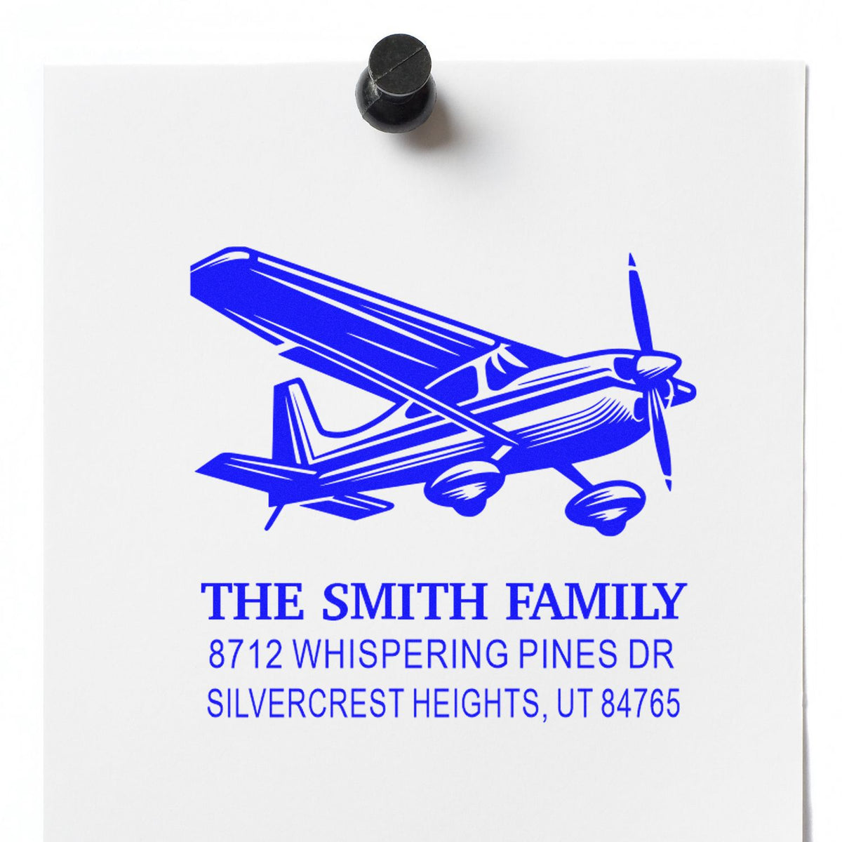 Blue custom address stamp with airplane graphic, The Smith Family name, and Utah address on white paper, shown with black stamp handle.