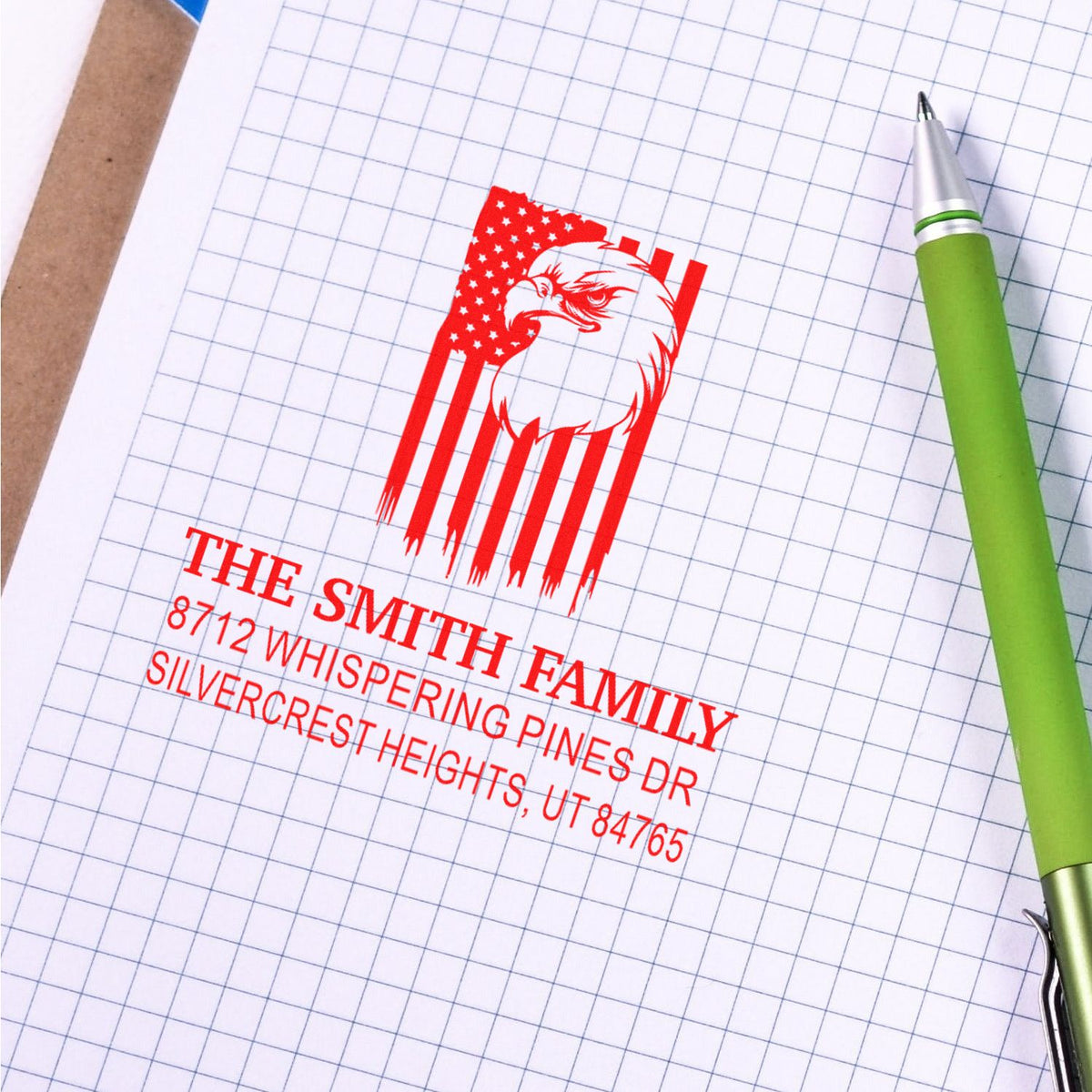 Custom address stamp with eagle and American flag design on graph paper beside a green pen, featuring The Smith Family address.