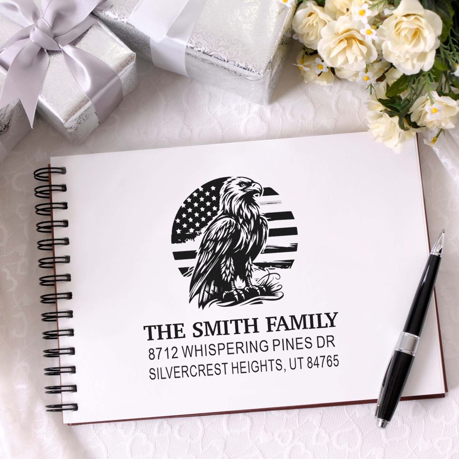 Custom personalized address stamp with eagle and American flag design stamped on a spiral notebook, styled with gift boxes, flowers, and a pen.