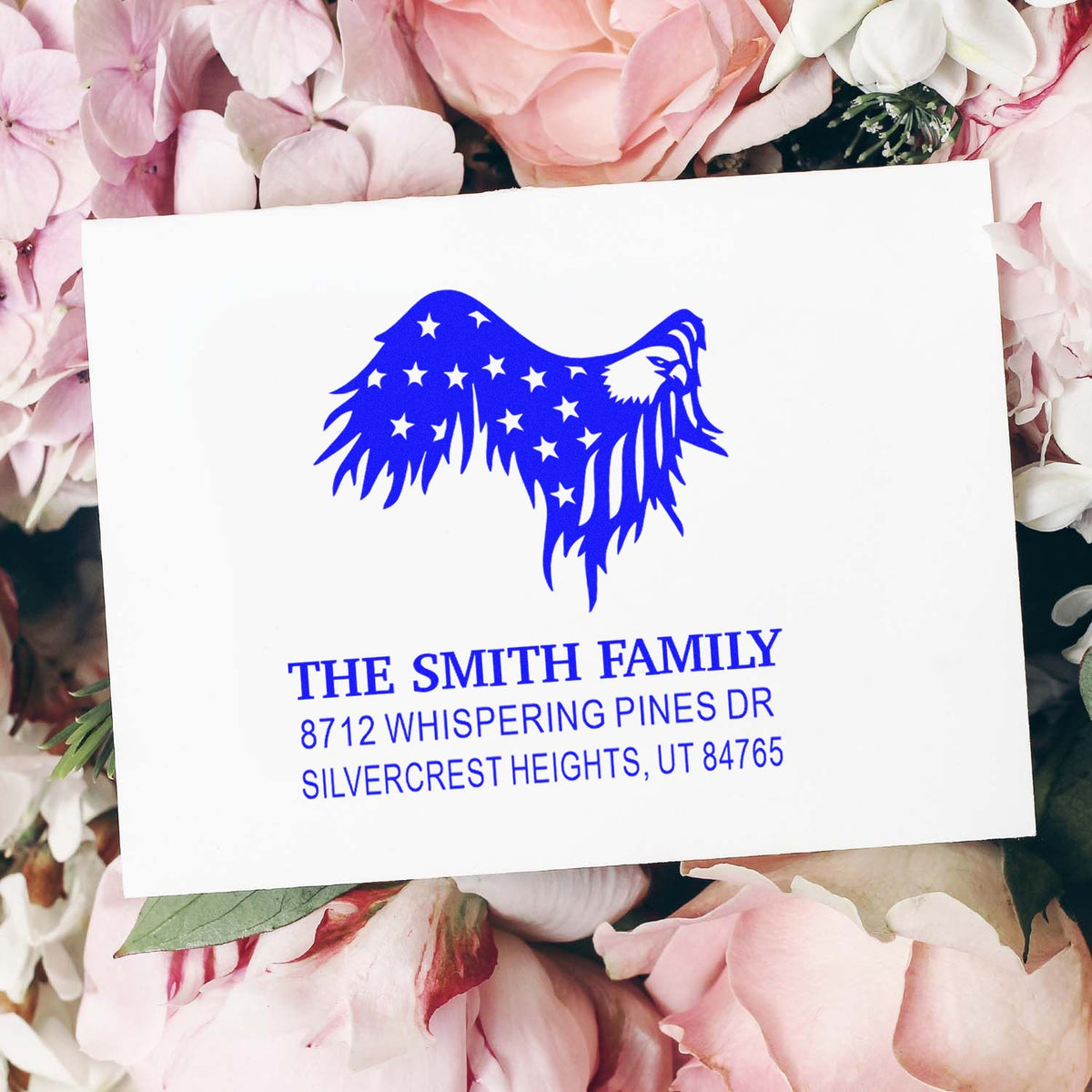 Custom blue family address stamp with eagle-and-stars design on white card, surrounded by pink flowers.