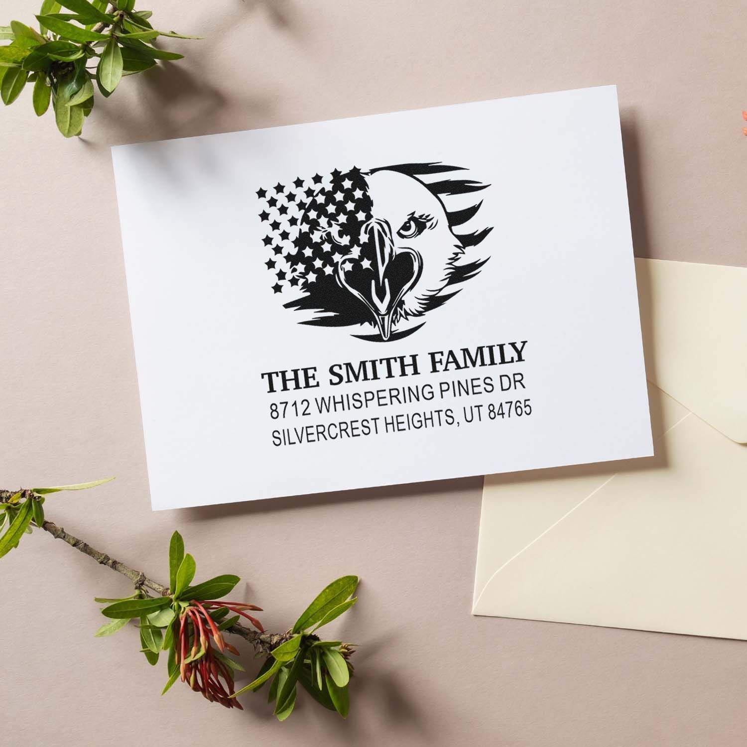 Custom family address stamp with eagle and stars design on white card, styled with envelope and greenery on a beige background.