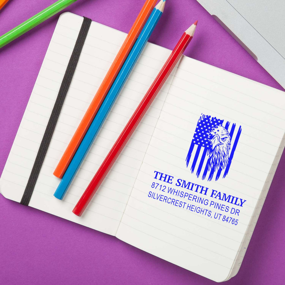 Custom address rubber stamp with eagle logo imprint on a notebook, featuring The Smith Family name and mailing address in blue ink on lined pages.