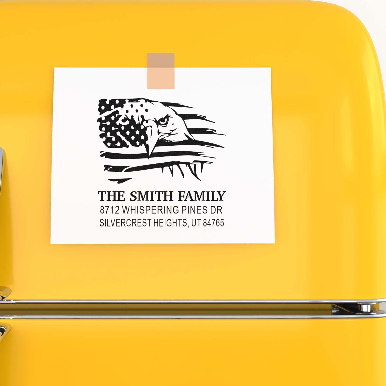 Custom self-inking family address stamp with eagle and U.S. flag design, taped to a bright yellow surface, reading The Smith Family, Silvercrest Heights, UT.
