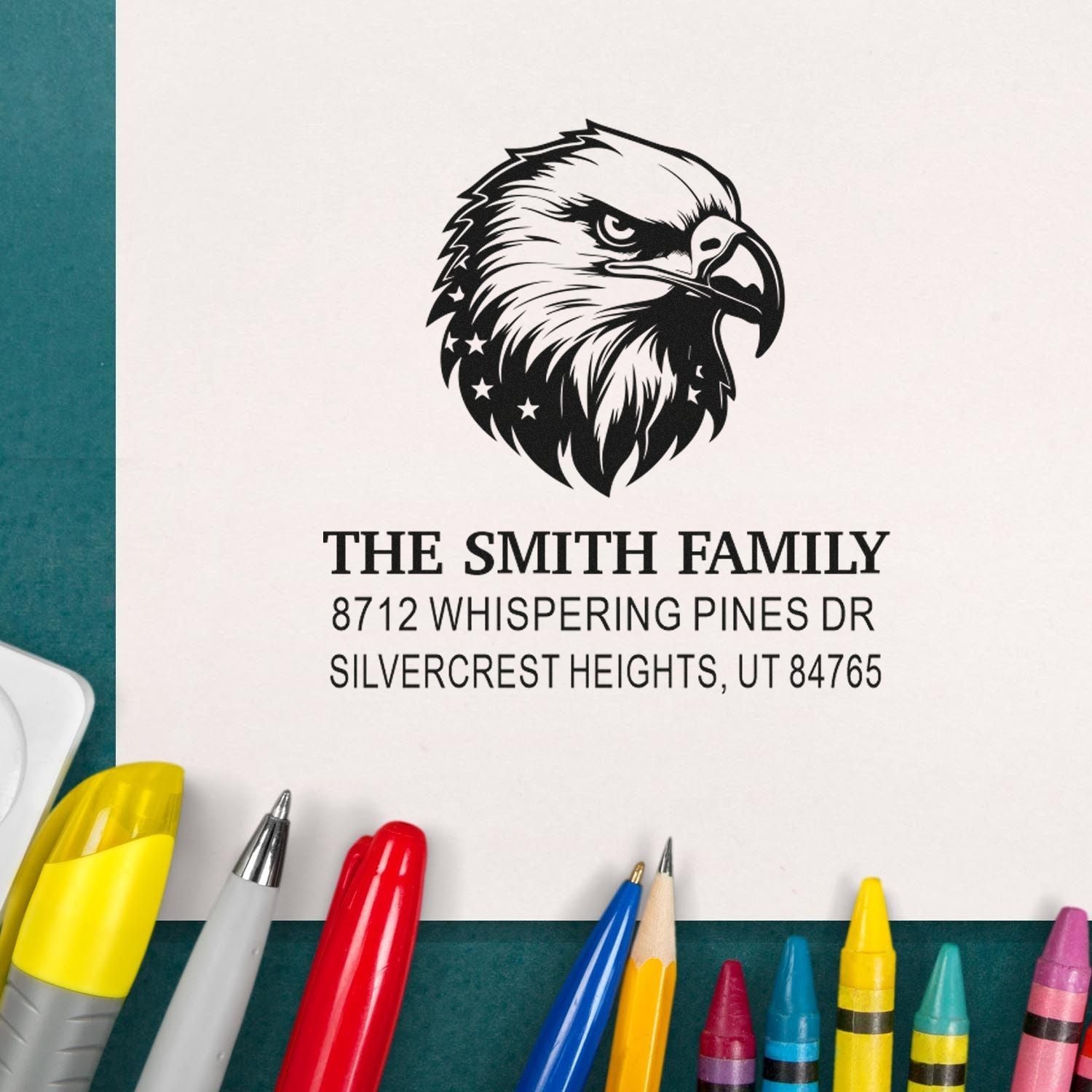 Custom address stamp with eagle logo for The Smith Family, shown on white paper with colorful pens on a teal background.