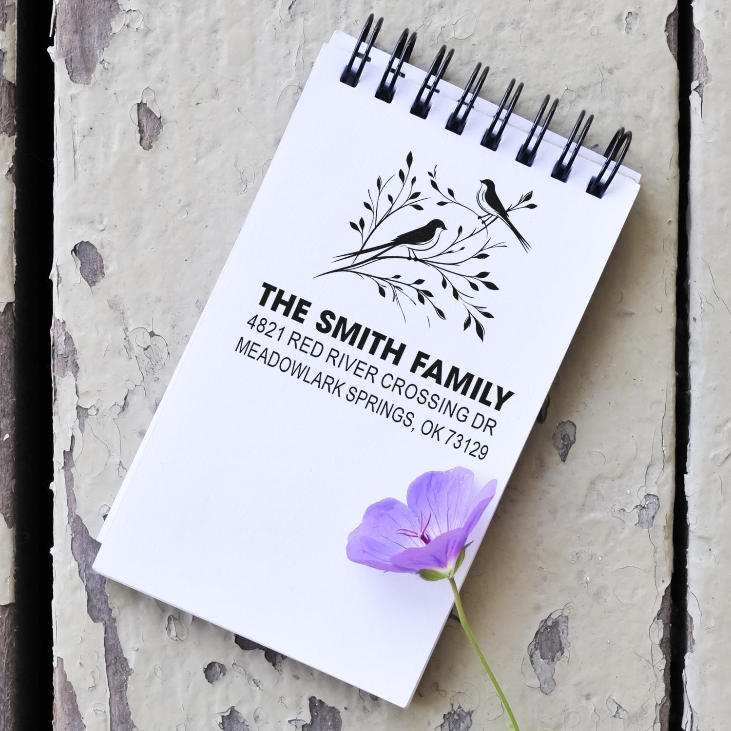 Custom rubber address stamp with bird design for The Smith Family, featuring name, street address, and floral accent on a notebook page.
