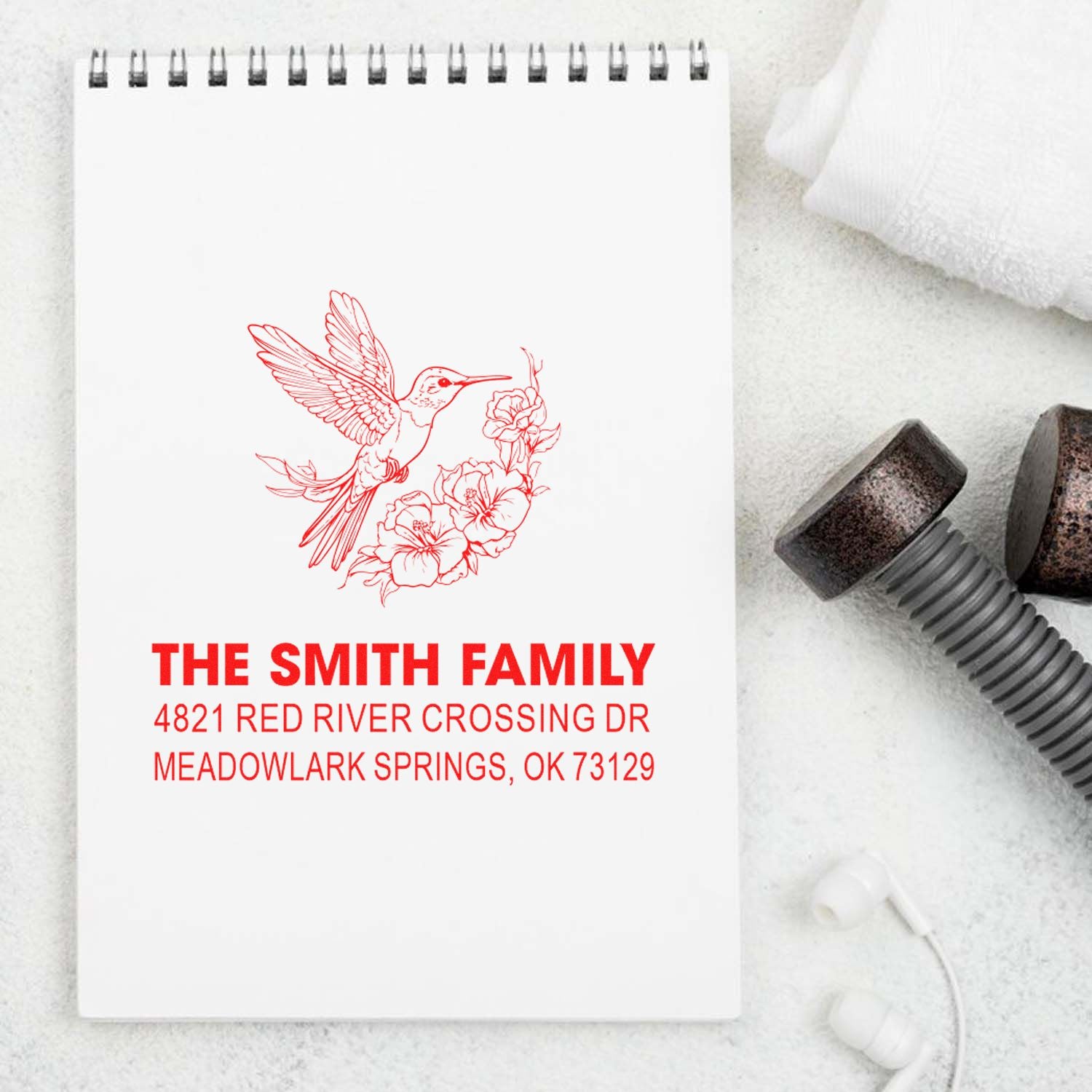 Personalized custom rubber address stamp with hummingbird and floral design for The Smith Family, showing return address on a spiral notebook.