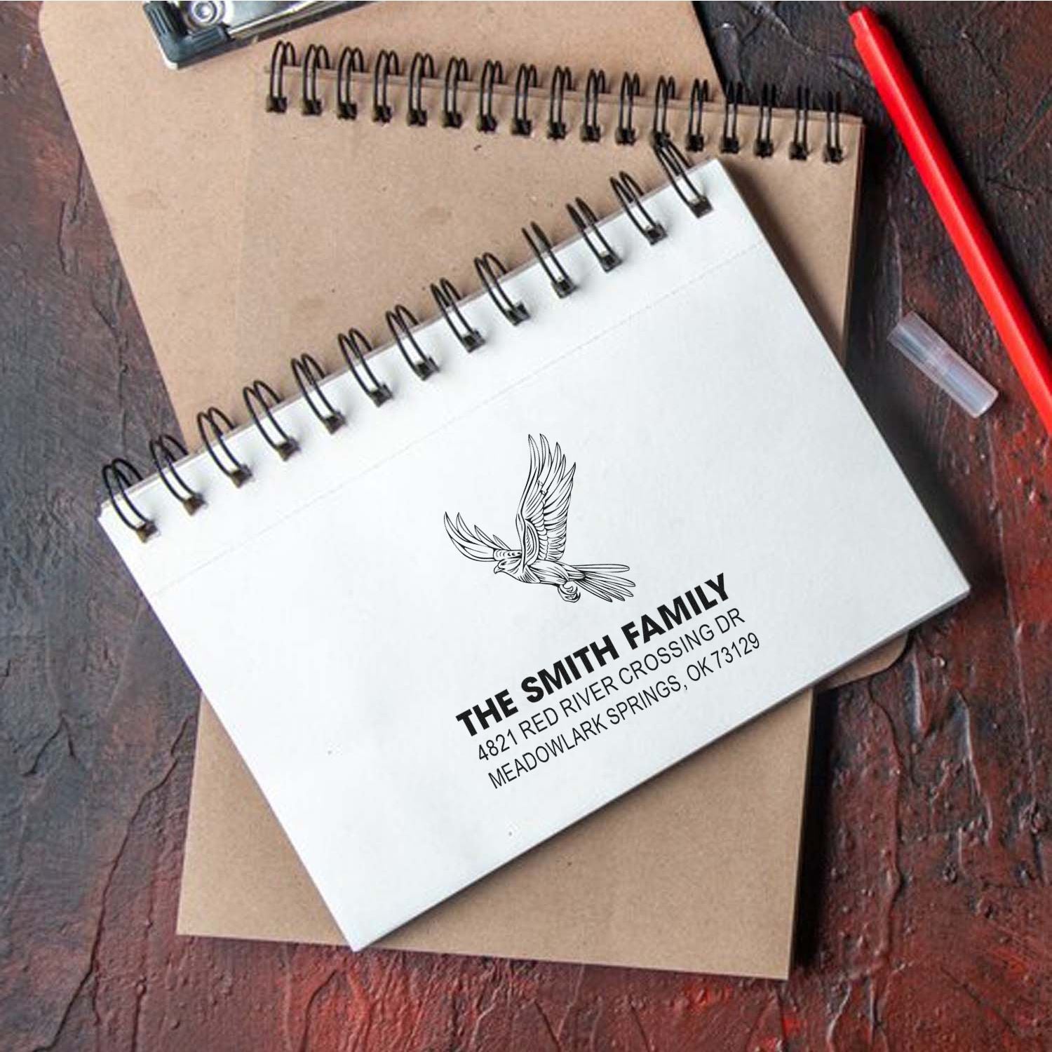 Custom return address rubber stamp with bird logo, personalized family name and address design on spiral notebooks, envelope and red pen