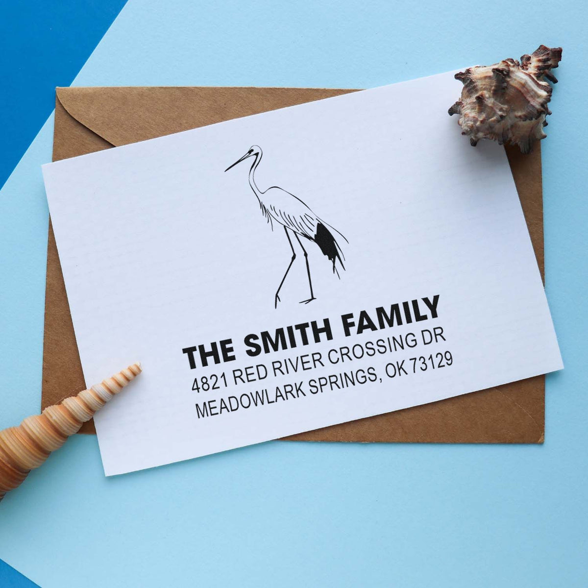 Custom rubber stamp return address with heron artwork for The Smith Family, printed on white envelope with kraft paper stationery and blue background.