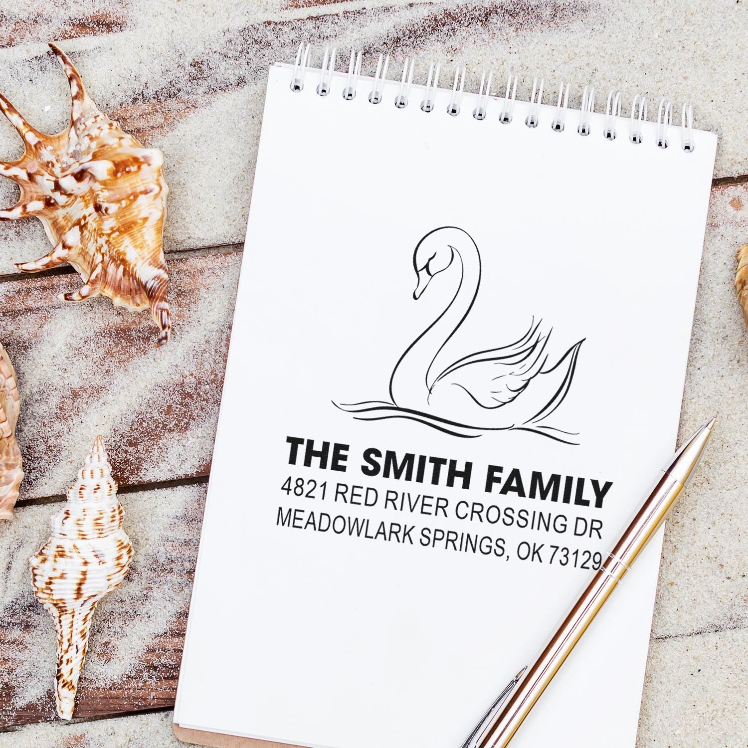 Custom swan family return address rubber stamp on a notepad, featuring personalized name and address with elegant beach-inspired design.