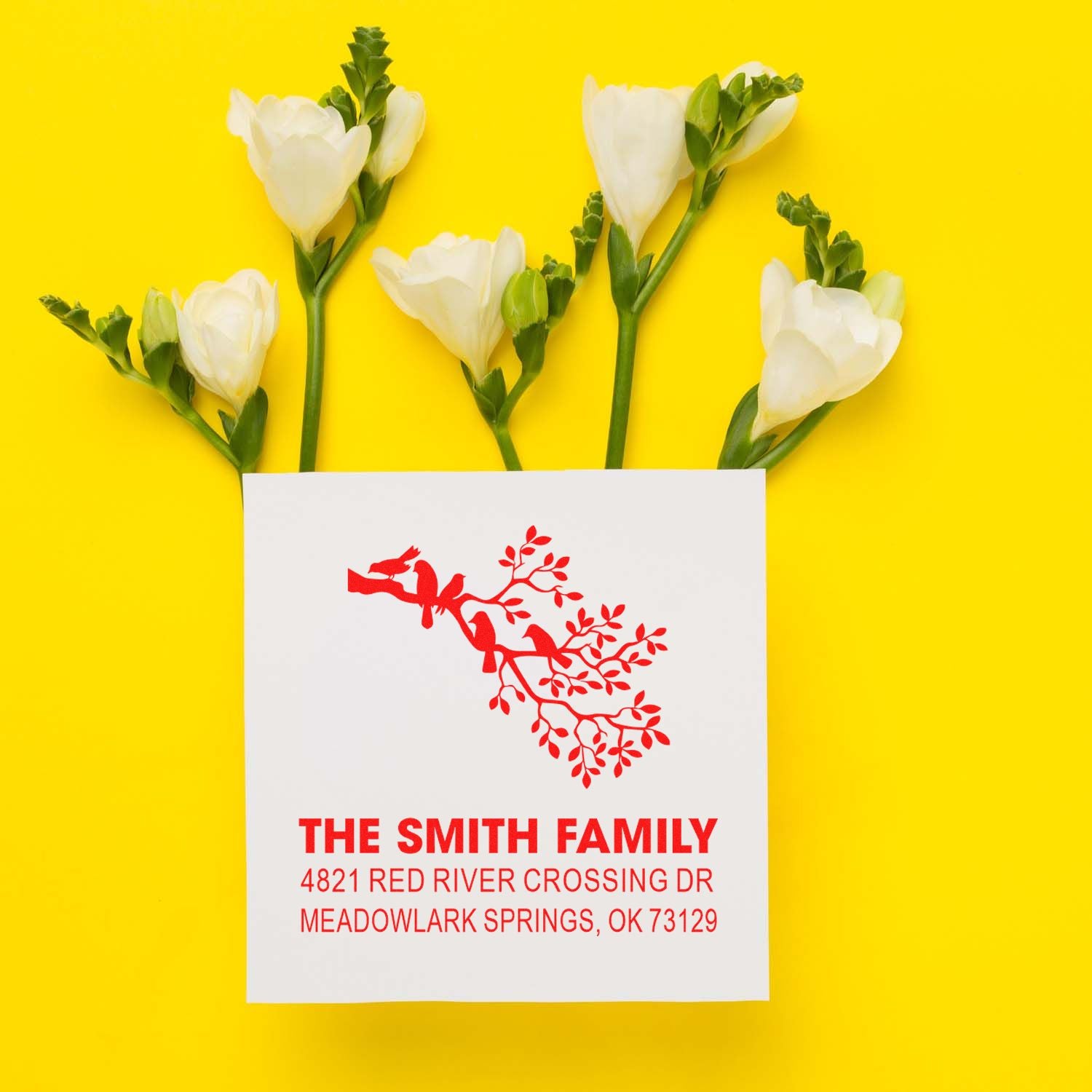 Custom family return address rubber stamp with red bird branch design, shown on white card with white flowers against bright yellow background.