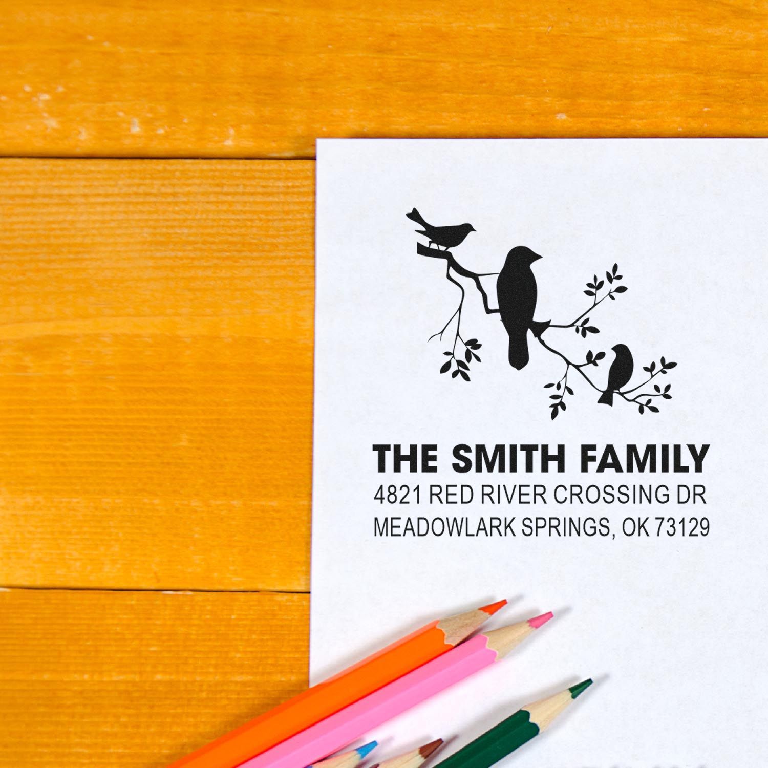 Custom address rubber stamp with bird branch design, The Smith Family name and Meadowlark Springs, OK address, shown on paper with colored pencils.