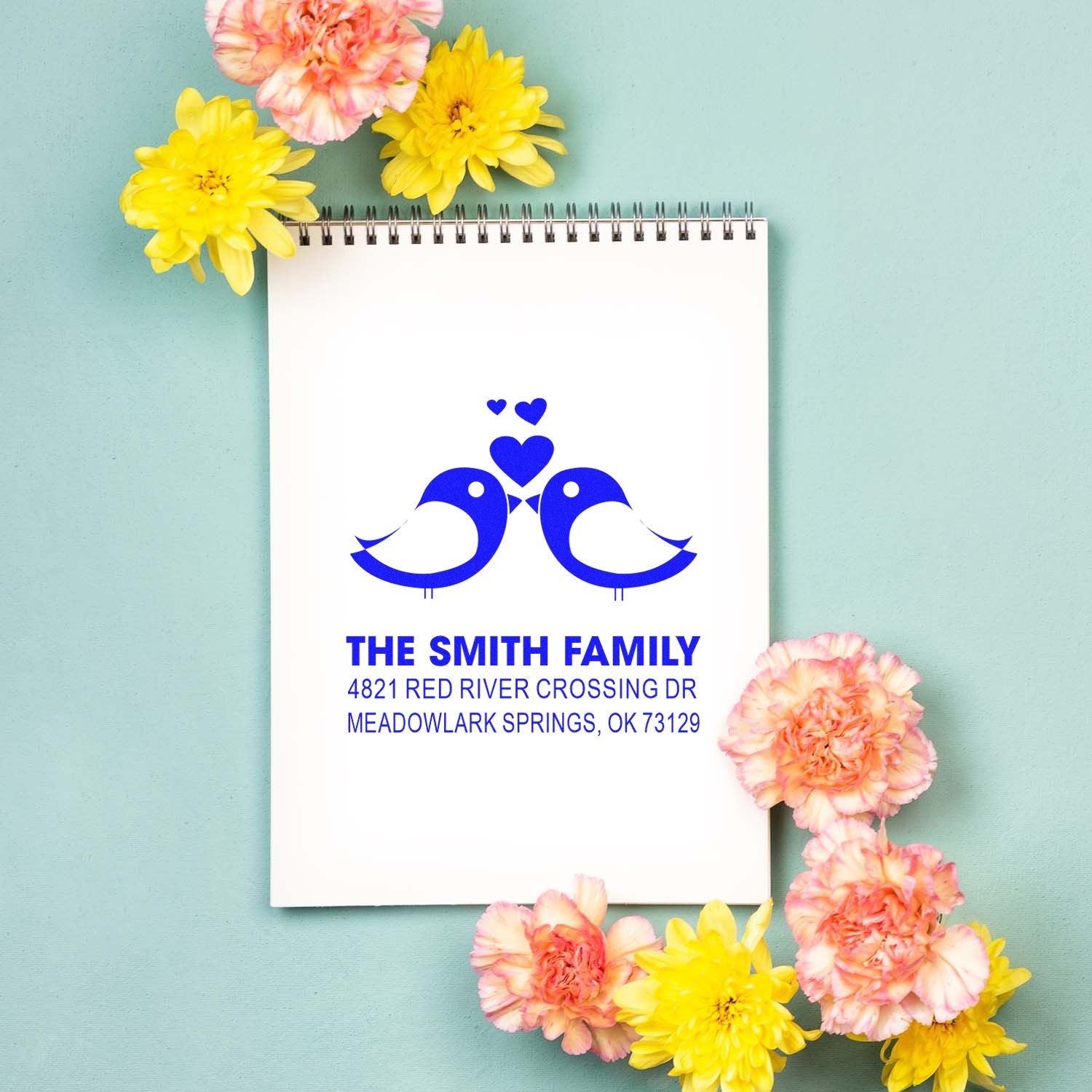 Custom return address rubber stamp with bird and heart design, blue ink on notebook, featuring The Smith Family address for wedding stationery