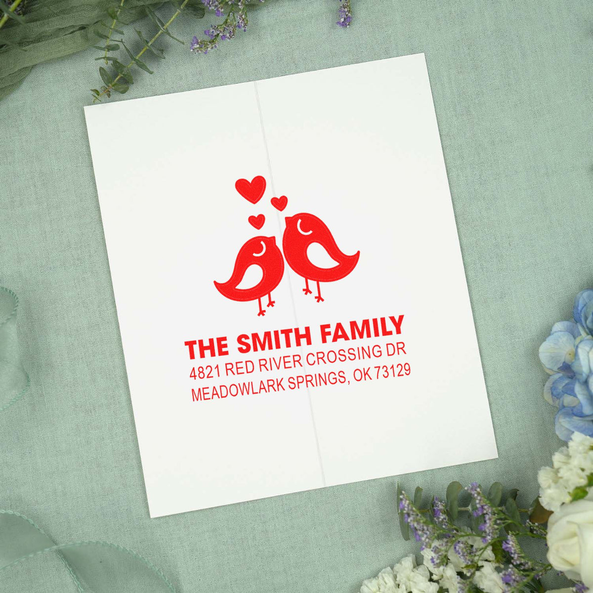 Custom rubber stamp with red lovebirds and hearts, personalized family name and return address for wedding stationery and mailing envelopes.