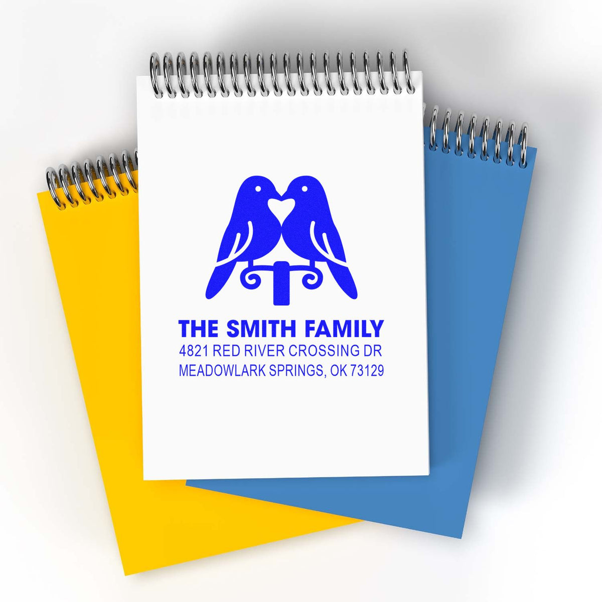 Personalized family address rubber stamp design with blue bird logo on spiral notebooks, featuring The Smith Family and Meadowlark Springs, OK for custom stationery