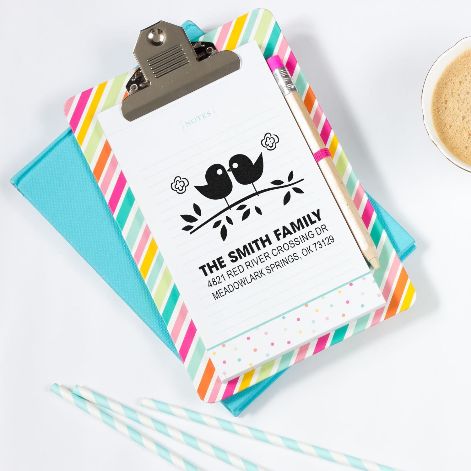 Personalized return address rubber stamp with bird design on lined notepad, styled on colorful clipboard with pen and stationery accessories.