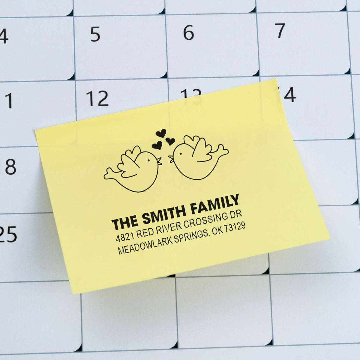 Custom return address rubber stamp with bird motif, personalized family name and mailing address on a yellow note over a calendar background.