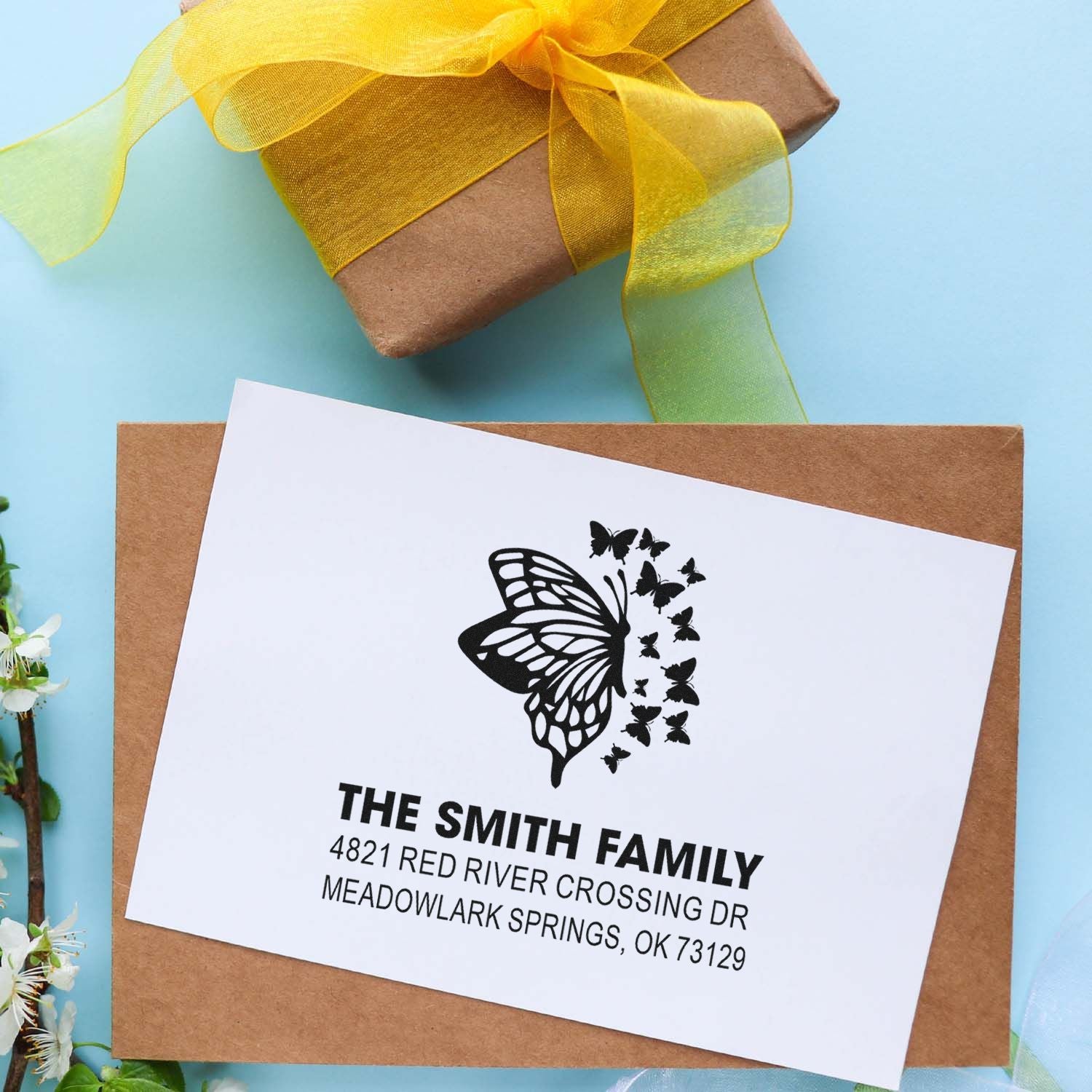 Custom butterfly return address rubber stamp on kraft envelope and gift box with yellow ribbon, featuring family name and mailing address