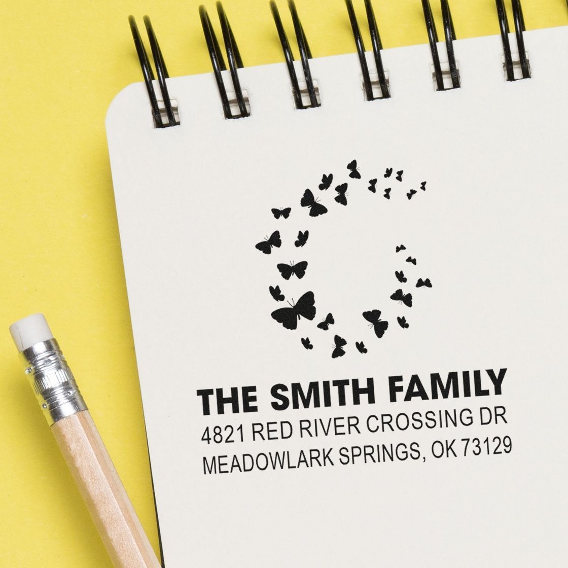 Custom butterfly monogram address rubber stamp on notebook, featuring The Smith Family name and return address for personalized mailing.