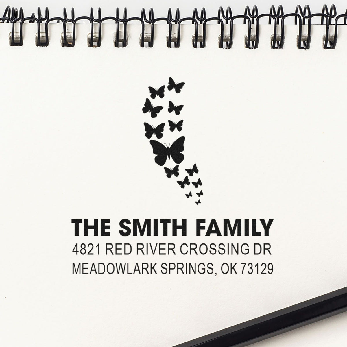 Custom butterfly family address rubber stamp impression on spiral notebook page featuring The Smith Family, 4821 Red River Crossing Dr, Meadowlark Springs, OK.