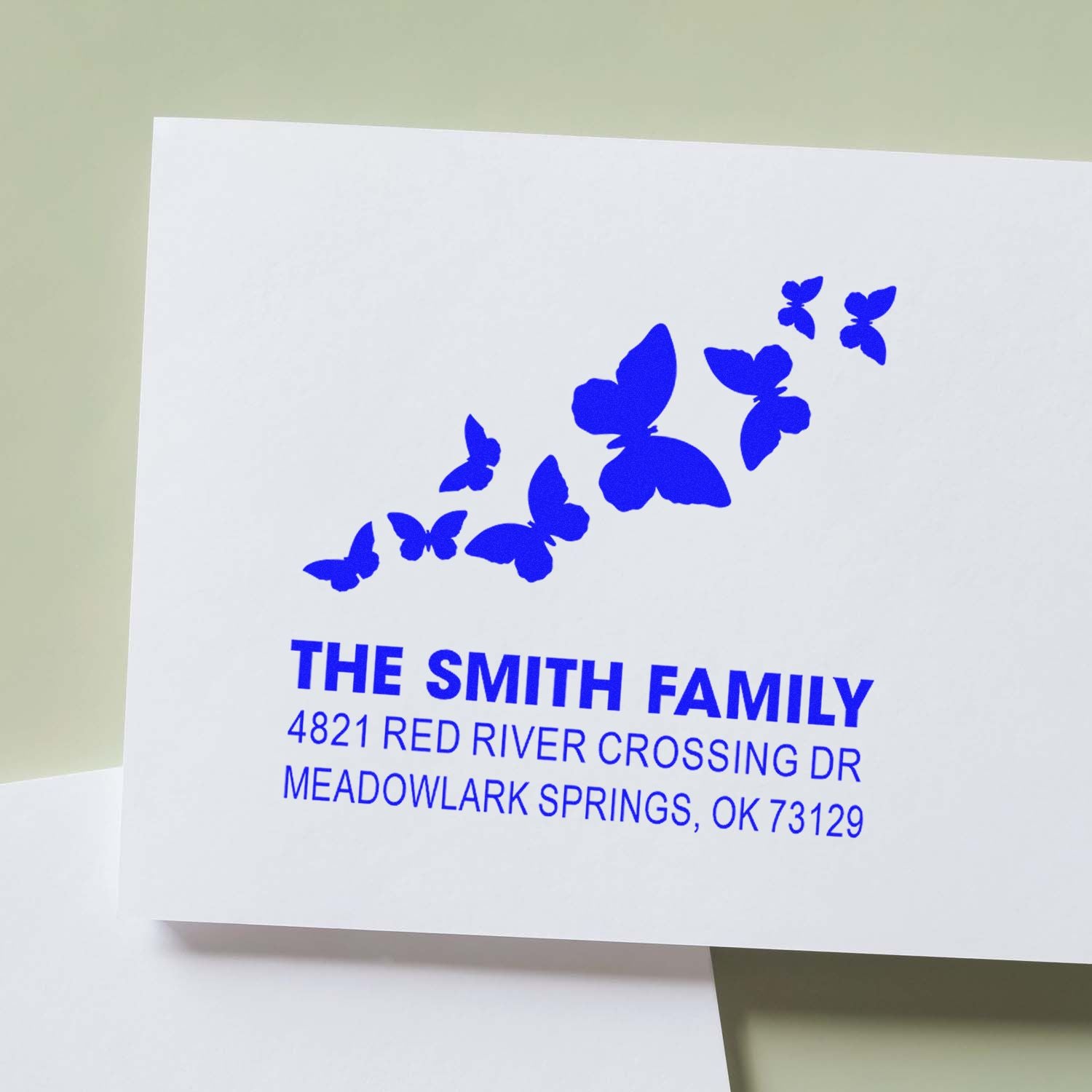 Custom butterfly address rubber stamp in blue ink with The Smith Family name and Meadowlark Springs, OK return address on white paper