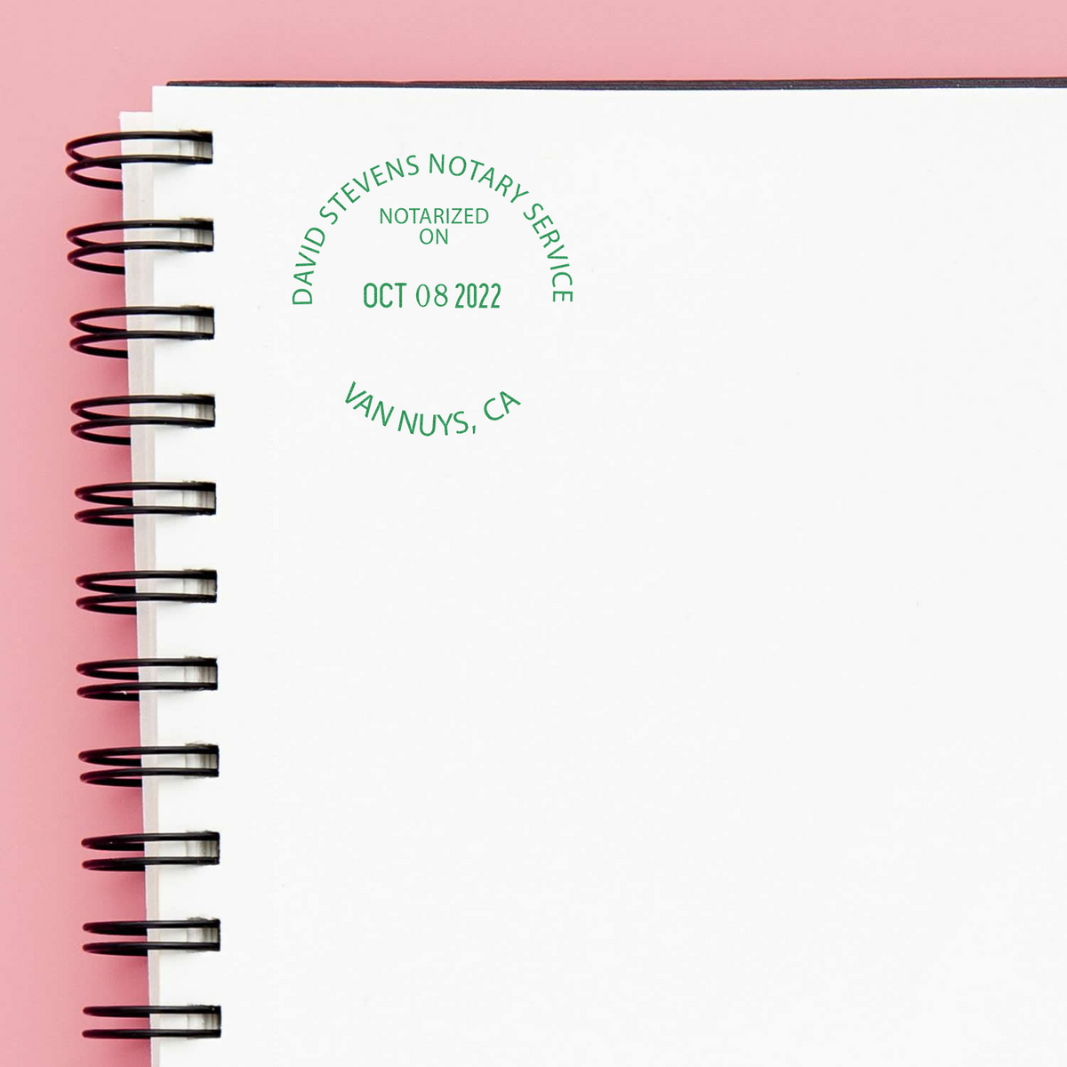 Spiral notebook with green notary stamp from David Stevens Notary Service on a pink background.