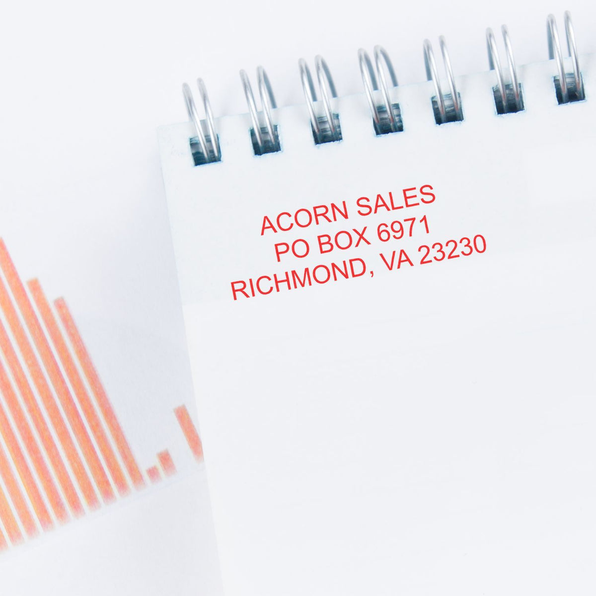 Close-up of spiral notebook with Acorn Sales mailing address and orange business chart graphic on white background.