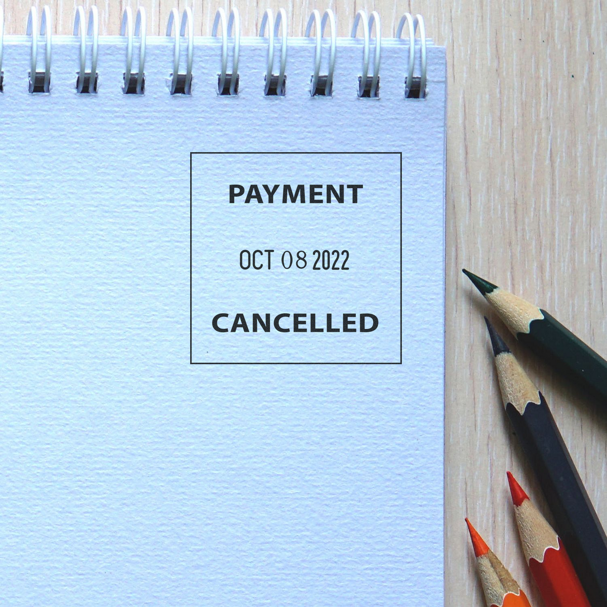 Notebook page with Payment Cancelled stamp and colored pencils on wooden desk.