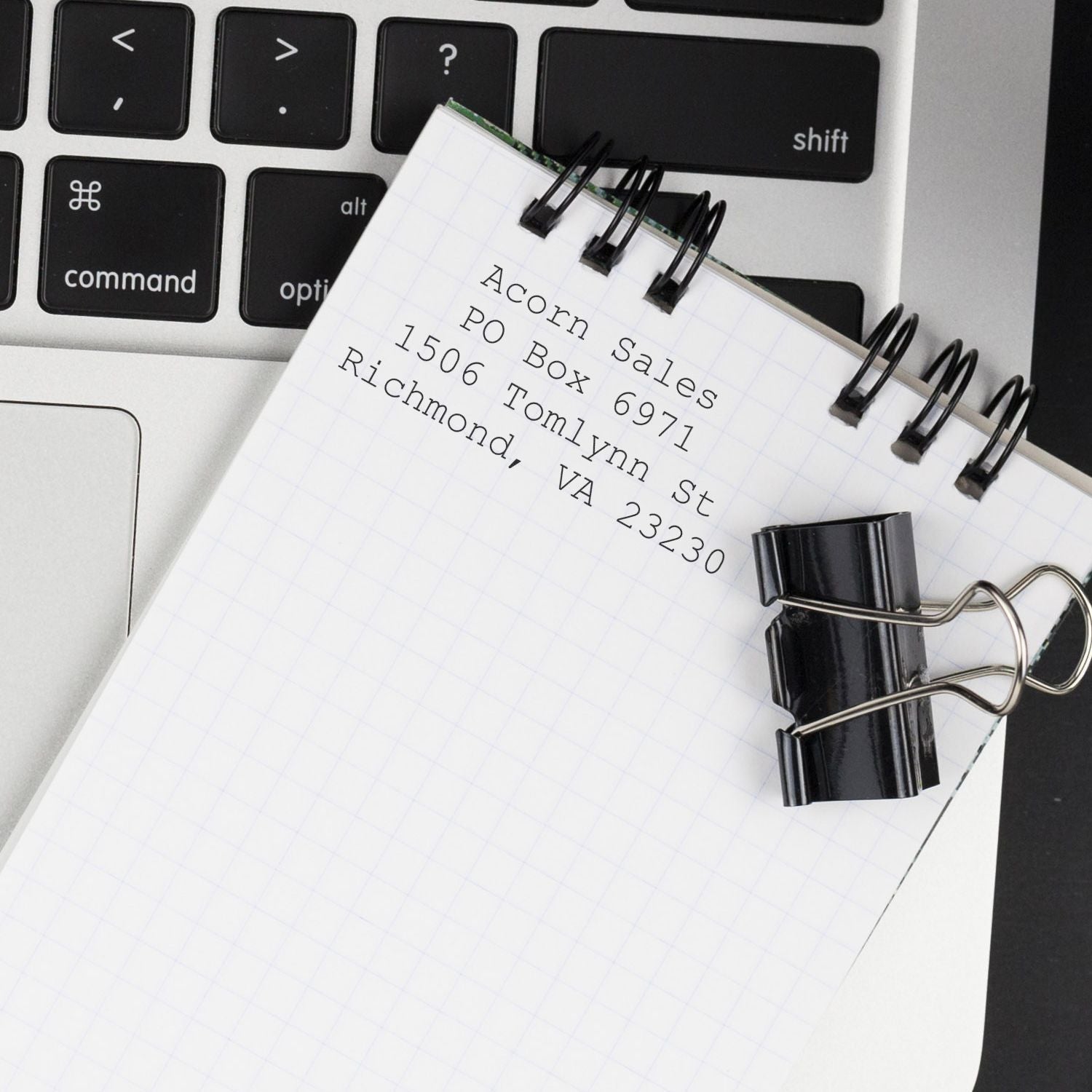 Notebook with printed mailing address clipped to a laptop keyboard, concept of contact information and office work.