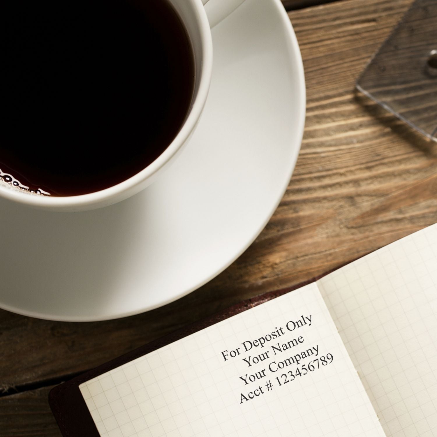 Close-up of a coffee cup beside an open checkbook with For Deposit Only printed on a wooden table.