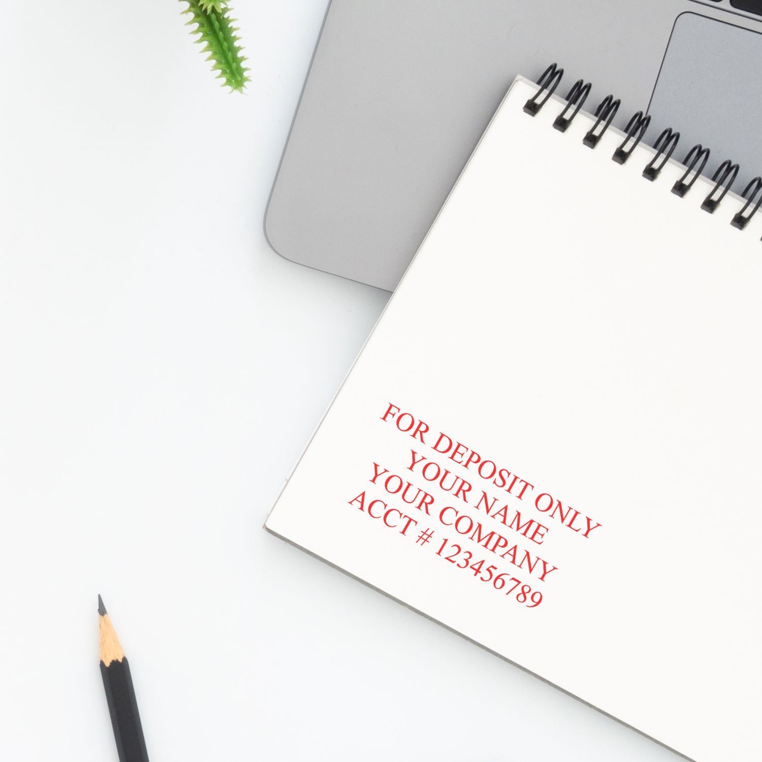 Close-up of spiral notebook with for deposit only note beside a laptop and pencil on a clean white desk.