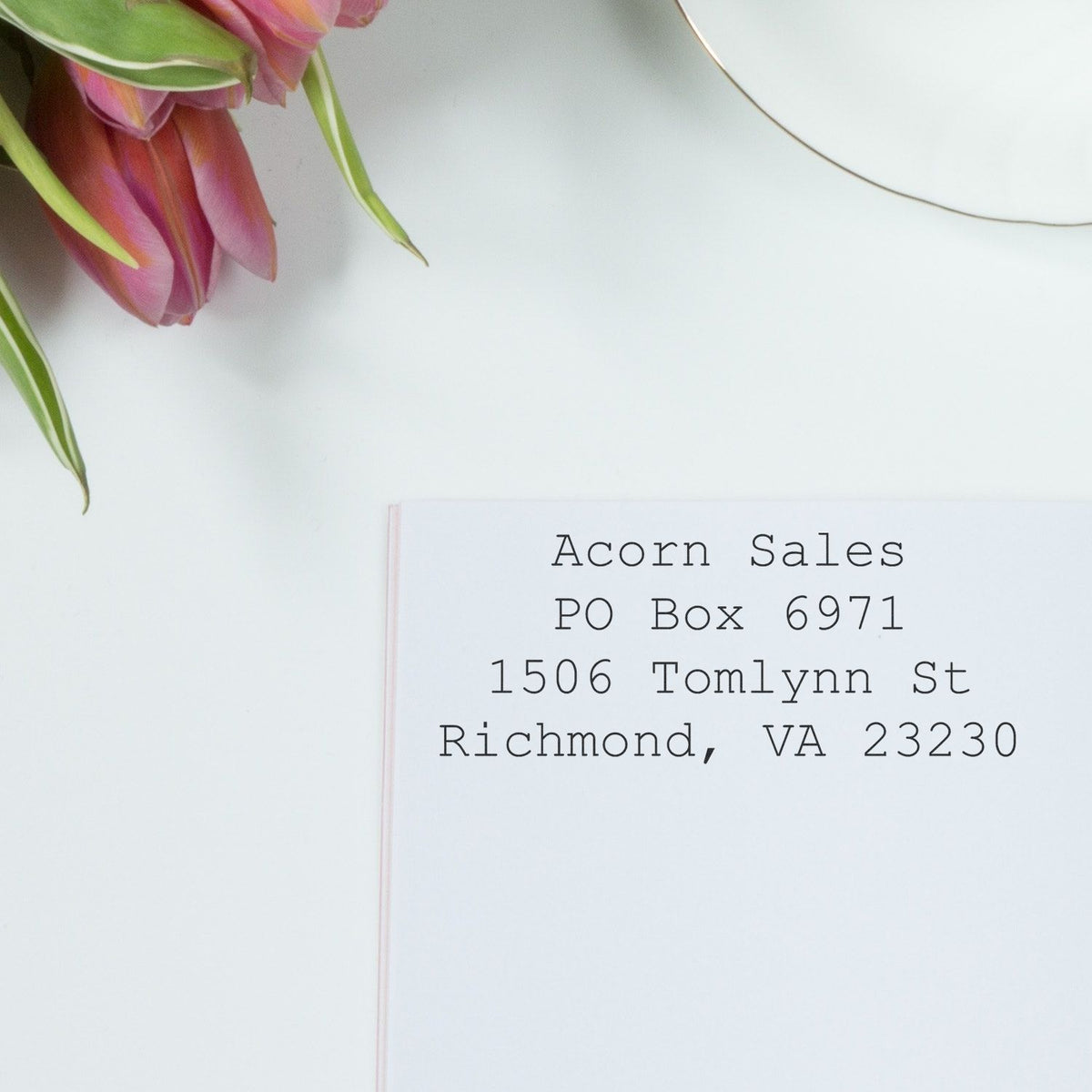 Personalized address label for Acorn Sales with pink tulips on a white desk background.
